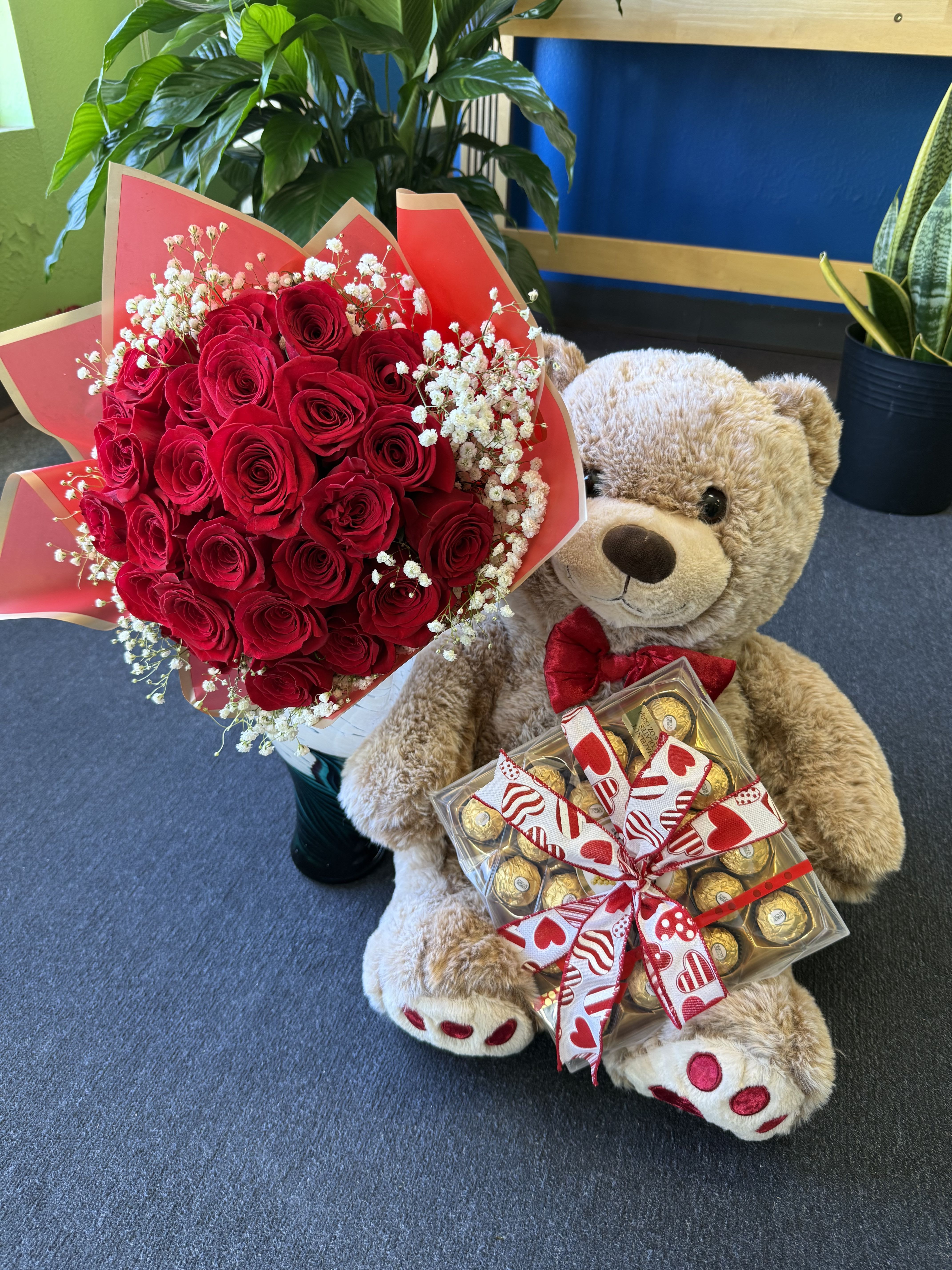 Red rose bouquet with baby’s breath beside a teddy bear holding chocolates
