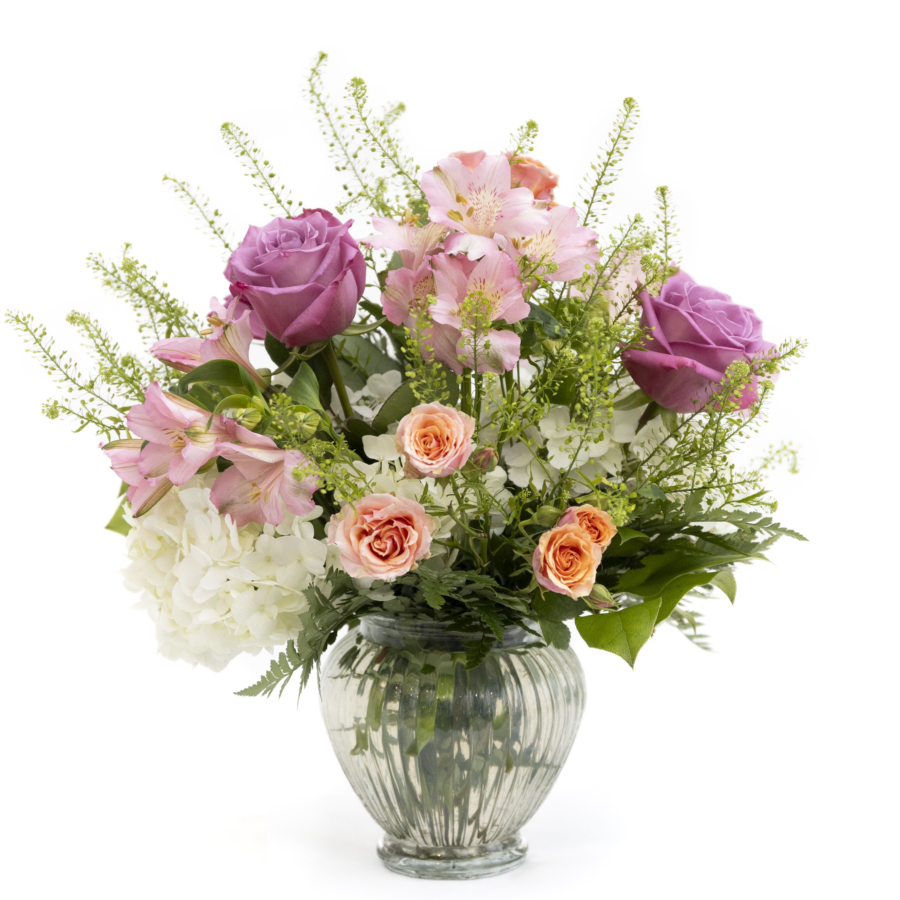Mixed bouquet of purple roses, peach spray roses and white hydrangeas in a clear glass vase