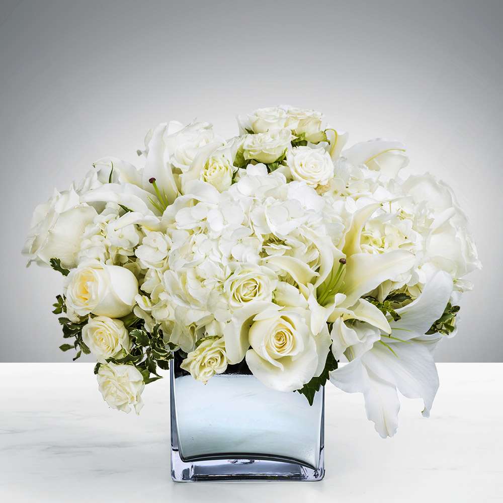 White roses and lilies arranged in a square glass vase