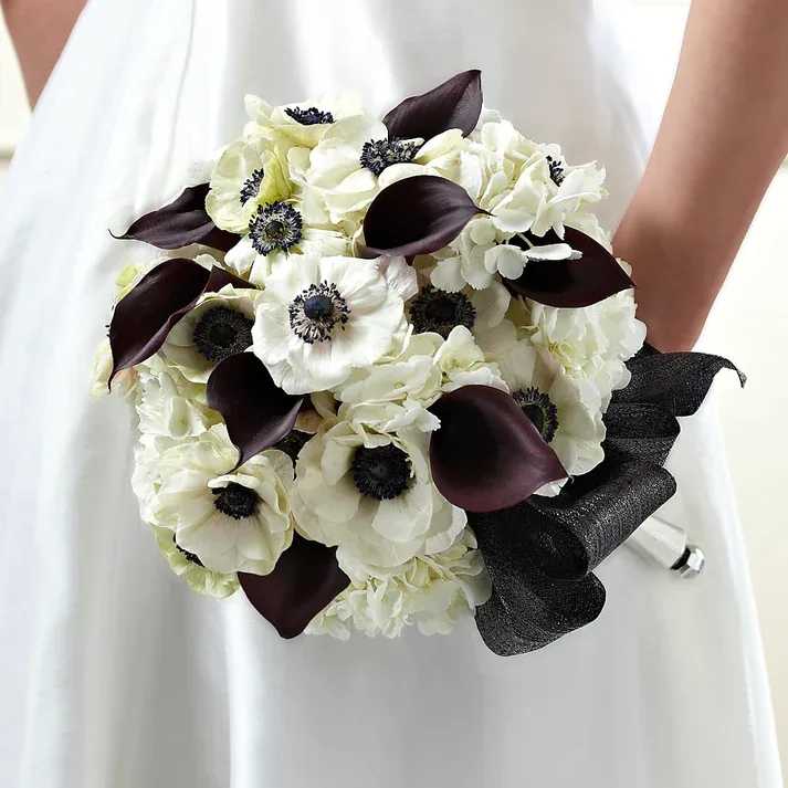 To Have and To Hold Bouquet - Chic, modern, and oh, so, sophisticated, this bridal bouquet is a simply stunning way to celebrate in style. Gorgeous white anemone stems pull focus with their white petals and black centers surrounded by dark plum mini calla lilies, and white hydrangea to create a stunning visual affect. Accented with black metallic ribbon to give it a bit of shine, and fitted into a silver metallic holder to add to the elegance of this piece, this bridal bouquet will look wonderful against your wedding dress.  Bouquet is approximately 12" H x 10" W