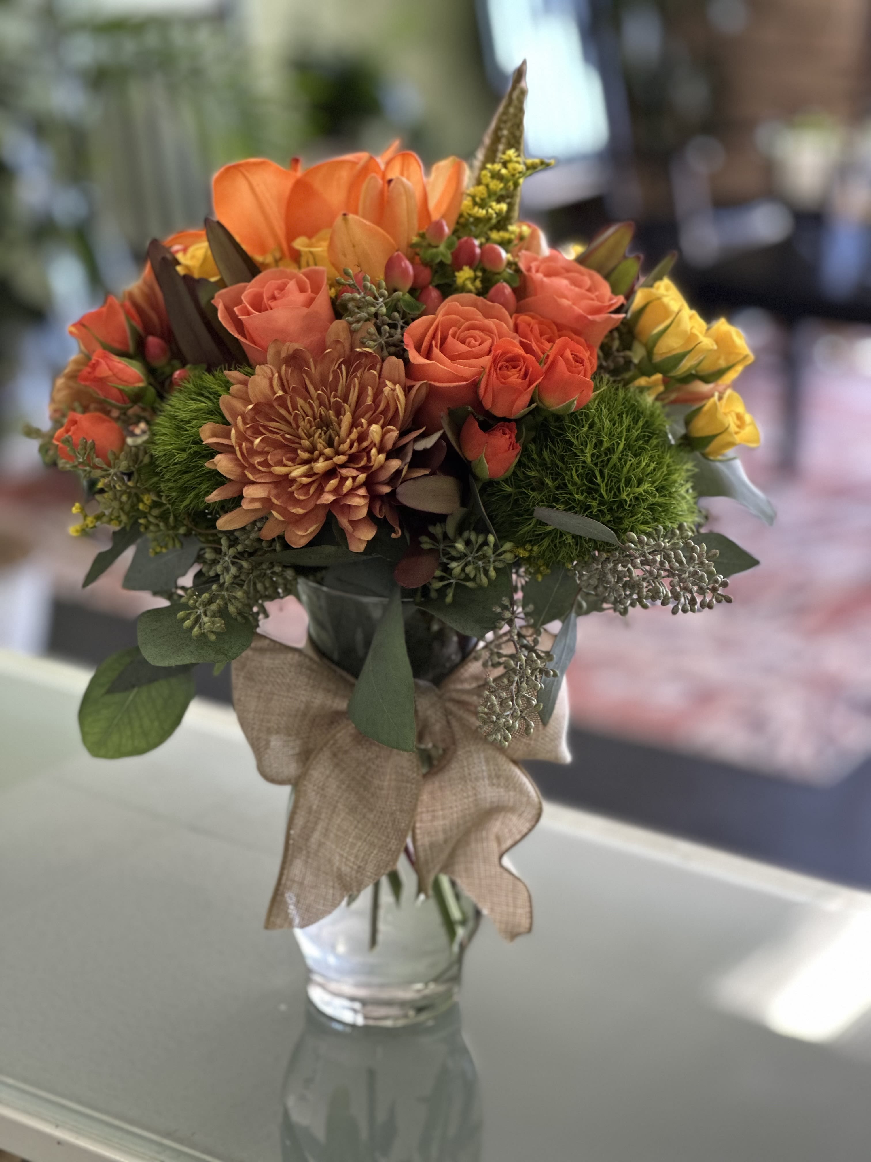 Orange and coral bouquet in a clear glass vase with a burlap ribbon