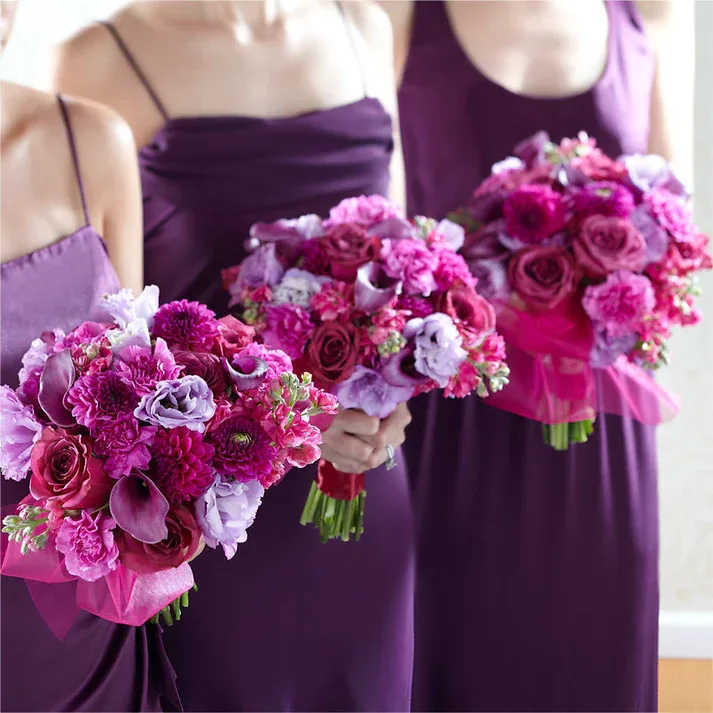 Bridesmaid's Garden Bouquet - On trend and set to celebrate, purple is the perfect choice! Your bridesmaids will love to walk down the aisle holding this exquisite bouquet which brings together plum mini calla lilies, fuchsia gilly flower, lavender carnations, plum dahlias, purple roses, and lavender double lisianthus arranged to create a dynamic and eye-catching affect. With the stems wrapped in a sheer burgundy ribbon, this bouquet is ready to make it's entrance.  Approx. 14" H x 7" W.