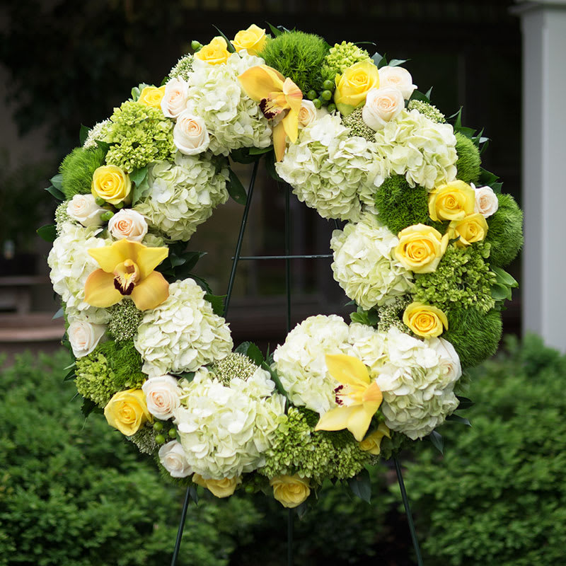 Yellow Remembrance - Yellow Remembrance Wreath | Wilmington, Delaware Funeral Flowers Celebrate a life filled with light and love with our Yellow Remembrance Wreath, a radiant funeral arrangement handcrafted by Petals Flowers and Fine Gifts in Wilmington, Delaware. This elegant standing wreath features lush white and green hydrangea, vibrant yellow roses, delicate yellow orchids, exotic white orchids, and green trichilium—all beautifully arranged on a standing easel to create a meaningful tribute for a funeral, memorial service, or celebration of life.  The Yellow Remembrance Wreath symbolizes warmth, friendship, and eternal peace. Its soft greens and bright yellow blooms offer comfort and hope while honoring the memory of someone dearly loved. The circular design represents everlasting love and remembrance, making it a perfect floral expression of sympathy and support.  As your trusted local florist in Wilmington, Delaware, we specialize in custom, high-quality funeral and sympathy flowers arranged with care and compassion. We offer same-day, tax-free flower delivery to all local funeral homes, churches, and residences in Wilmington, Newark, Hockessin, Chadds Ford, Glen Mills, Kennett Square, and nearby areas.  Why Choose Petals Flowers and Fine Gifts?  * Luxury, custom-designed funeral and memorial arrangements * Locally owned flower shop in North Wilmington with personalized service * Same-day, tax-free delivery across Wilmington and surrounding communities