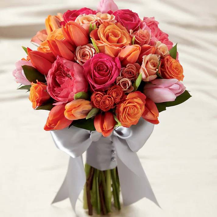 Sunset Dream Bouquet - Our Sunset Dream Bouquet bursts with sun-drenched color to captivate and charm at every turn. Orange tulips, peach spray roses, pink garden roses, fuchsia roses, light orange tulips, light pink tulips and orange spray roses are brought together to create an eye-catching look. Tied together at the stems with a wide silver gray satin ribbon, this bouquet speaks of love's unending emotion.  Bouquet is approximately 12" H x 9" W