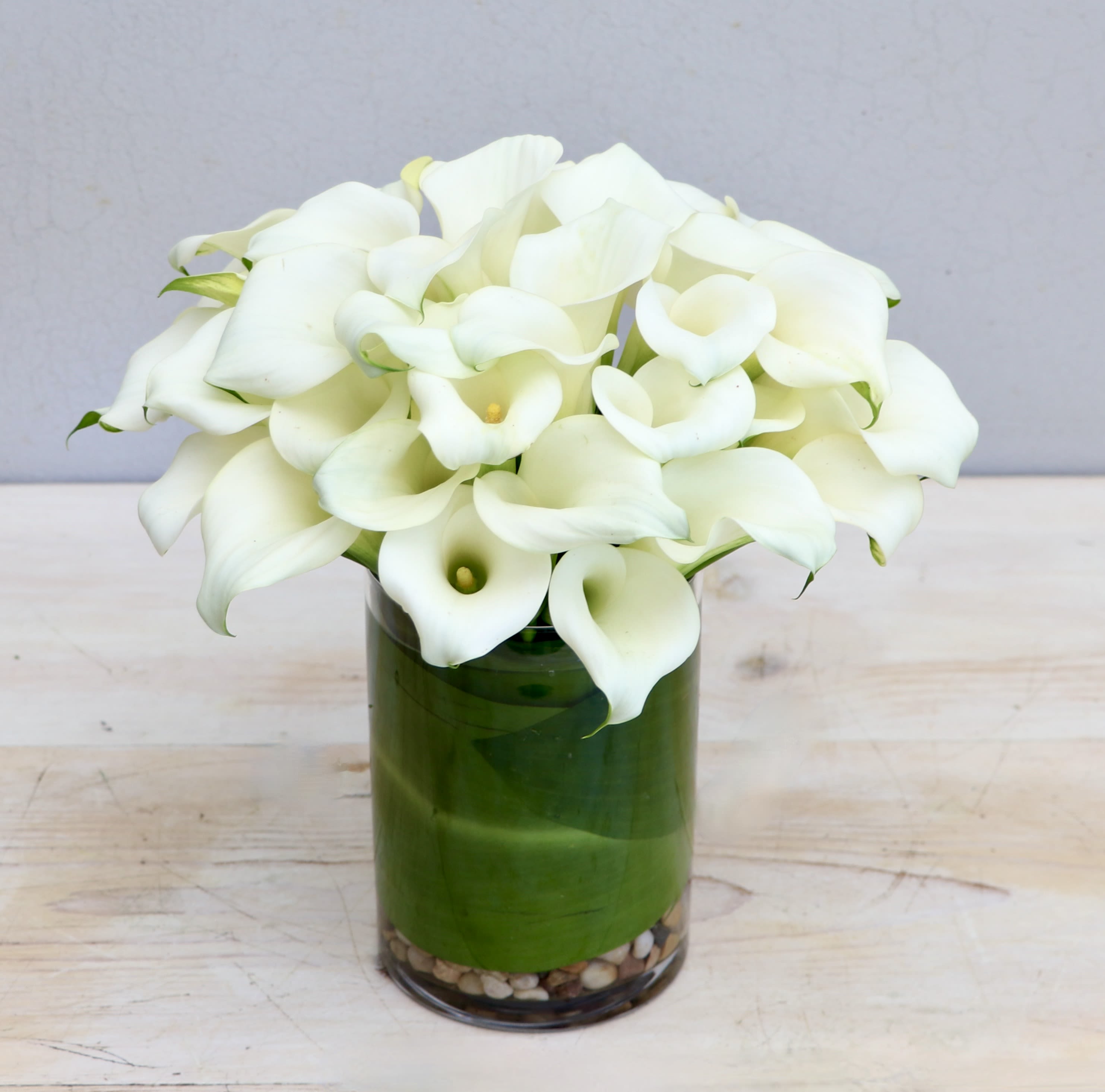 Calla Love - My Glendale Florist  - This arrangement showcases calla lilies in a glass vase with ti leaf lining. The standard size comes with 30 callas, each upgrade comes with 20 more. Don't forget to upgrade for more blooms! 