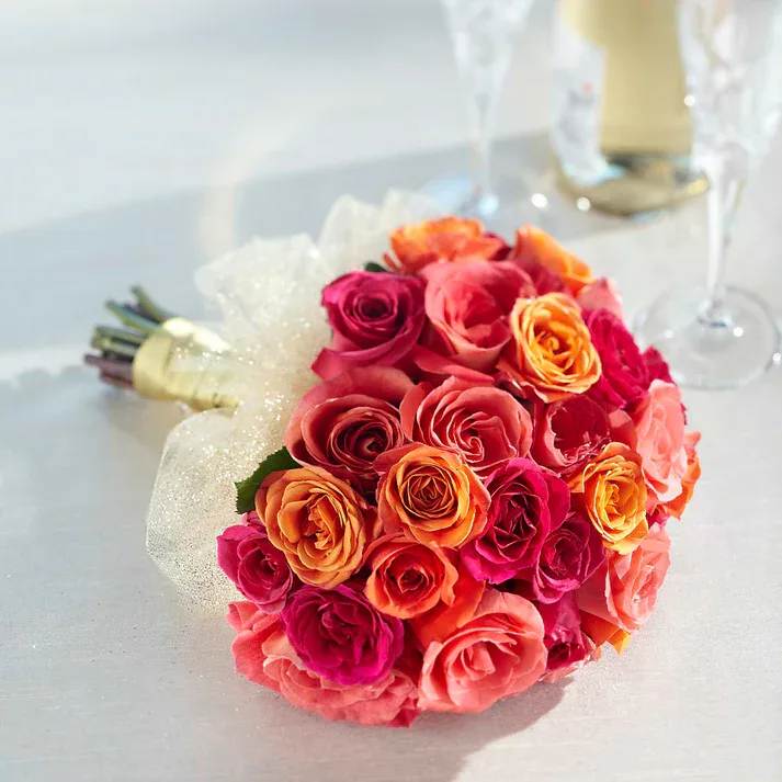 Sweet Roses Bouquet - Sunkissed, warm, and swirling with a beauty that only comes from a collection of roses, this gorgeous bridal bouquet is an exquisite choice. Bringing together hot pink, coral, orange, and bi-colored pink and peach roses and spray roses, this bouquet has been designed by a floral expert to blend the colors into the perfect hand-tied bouquet. Tied at the stems with gold grosgrain ribbon and accented with gold sparkle tulle at the base of the blooms, this bouquet brings sunlit magic to your wedding day.  Bouquet is approximately 12" H x 9" W