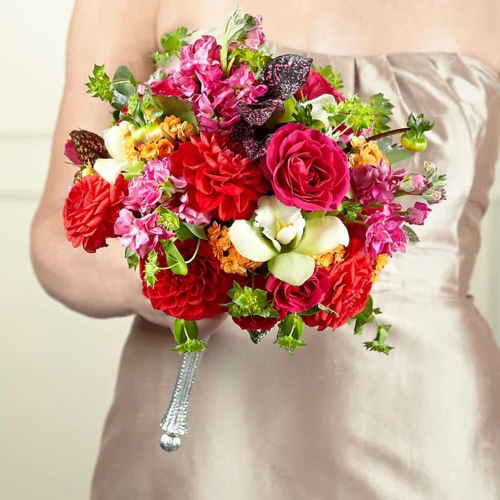 True Happiness Bouquet - Blending all of the right textures and colors together in just the right places, this captivating bridesmaid bouquet has a garden gorgeous appeal to it that never goes out of style. Burnt orange dahlias, pink gilly flower, hot pink spray roses, green Cymbidium Orchids, orange kalanchoe, bupleurum, and speckled pink fittonia leaves are brought together to form a simply stunning display. Arranged to fit a silver metallic bouquet holder to add even further glamour to this piece, this bouquet is ready to get your wedding day started in style.  Bouquet is approximately 12" H x 10" W