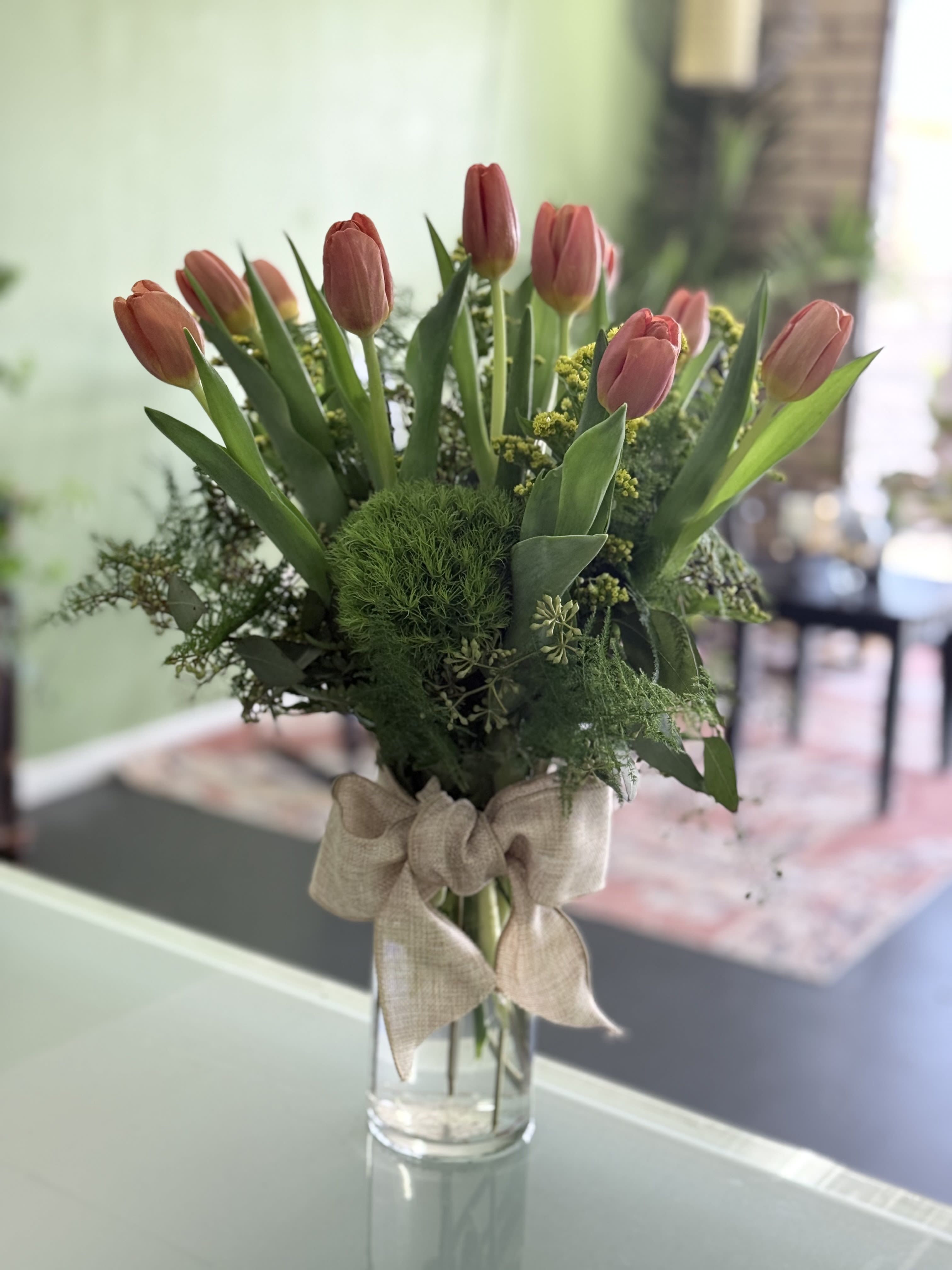 Pink tulips arranged in a clear glass vase with a burlap bow