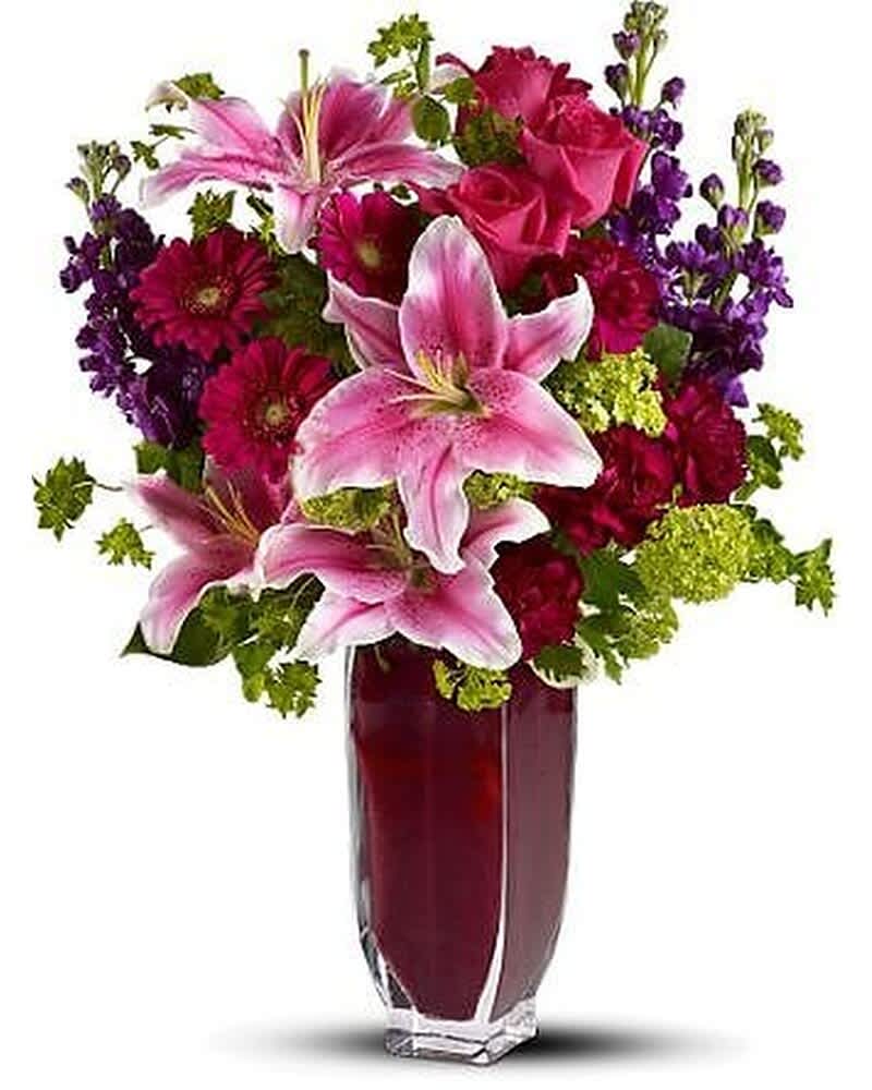 Tall arrangement of pink lilies, red roses, purple blooms and green accents in a clear glass vase
