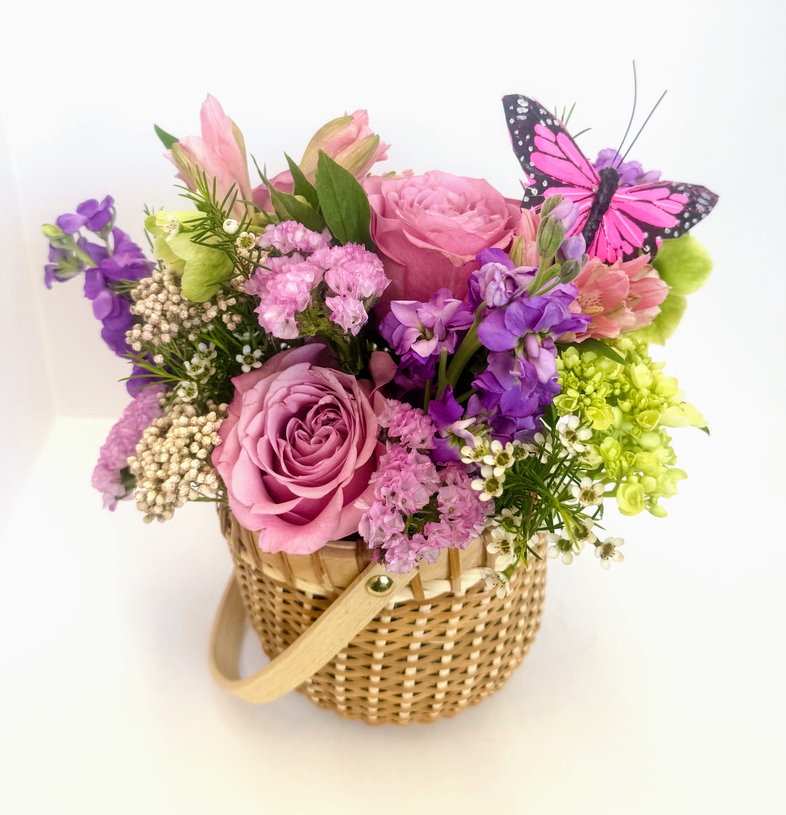 Nantucket Mother's Day Basket  - A Mother's Day arrangement in a Nantucket basket with purple roses, green hydreas, alstroemeria, white wax flower, rice flower and helleborus  