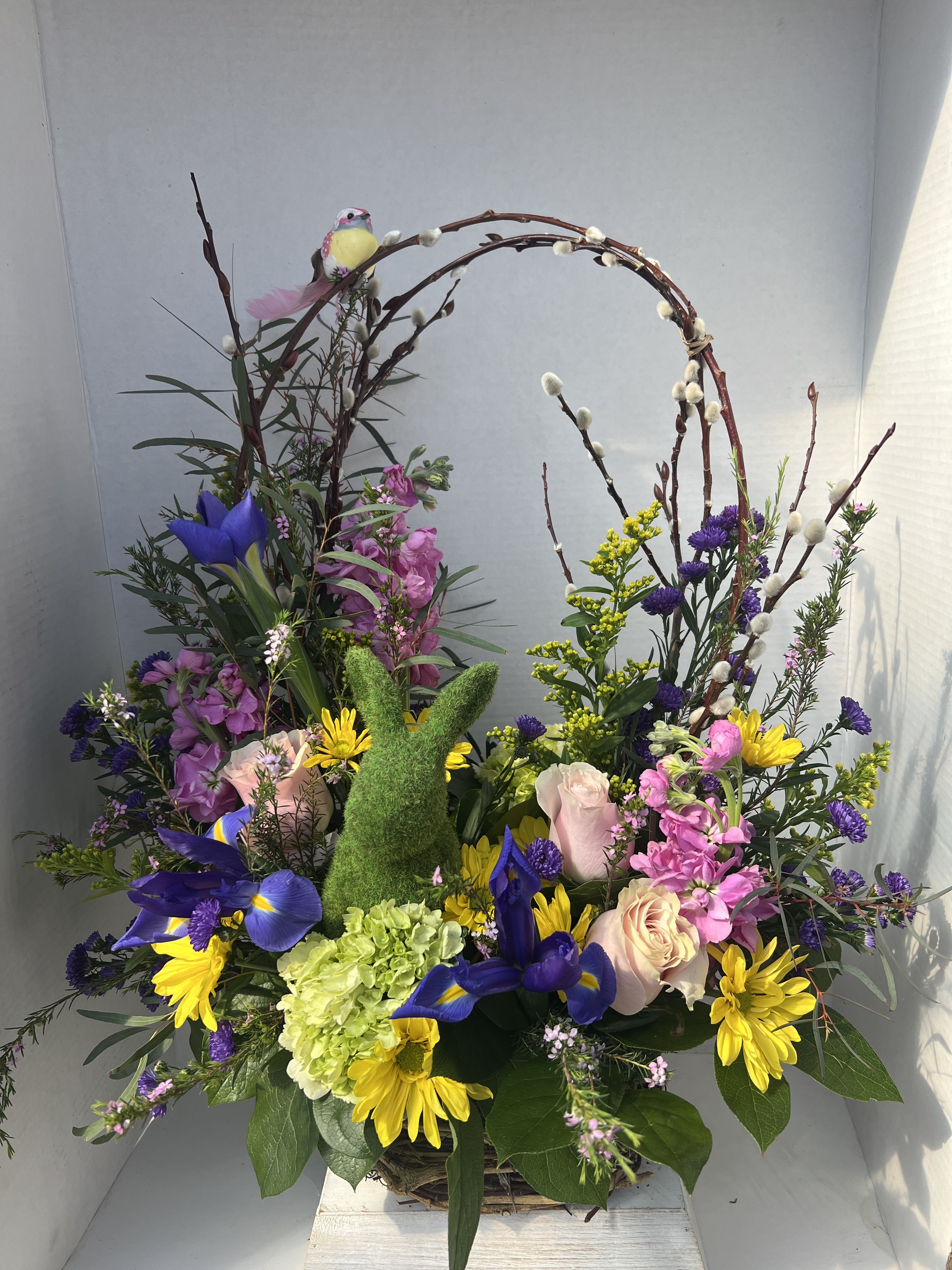 Happy Spring Time - Hoppy Spring is a whimsical spring basket bursting with cheerful color and charm. This delightful arrangement features a lively mix of pink, yellow, and purple spring blooms, artfully gathered to capture the fresh, happy spirit of the season. At the heart of the basket sits an adorable mossy bunny, nestled among soft greenery and playful textures. Graceful pussy willow branches rise above the flowers, adding a touch of natural elegance and a hint of early spring magic.
