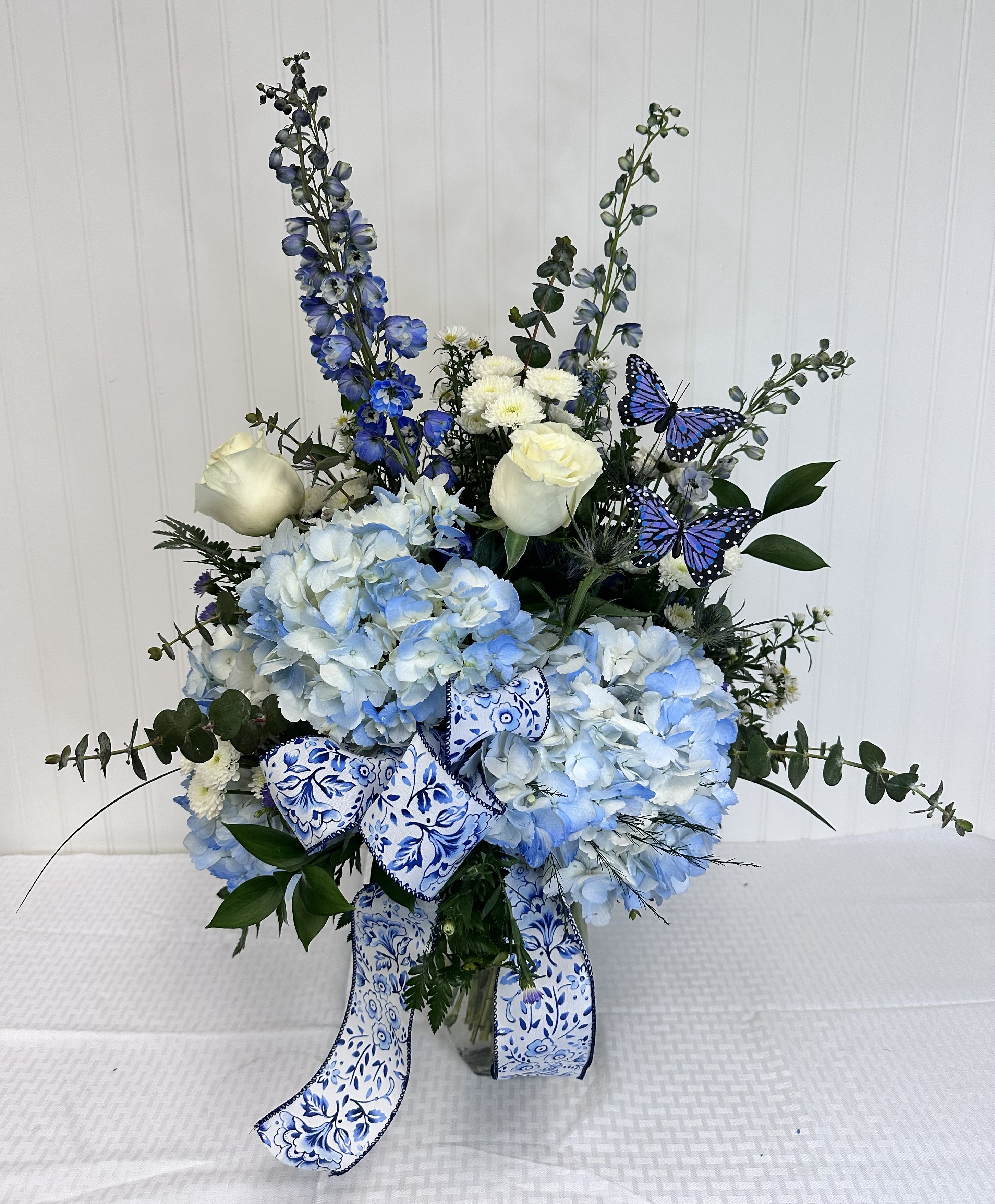 The Sonya - The Sonya is an elegant Mother's Day arrangement made solely of Blue &amp; White. In this creation you will get: Blue Hydrangea's, White Roses, Delphinium, Blue Thistle, and white accent flowers. The finishing touches include butterflies and matching bow.