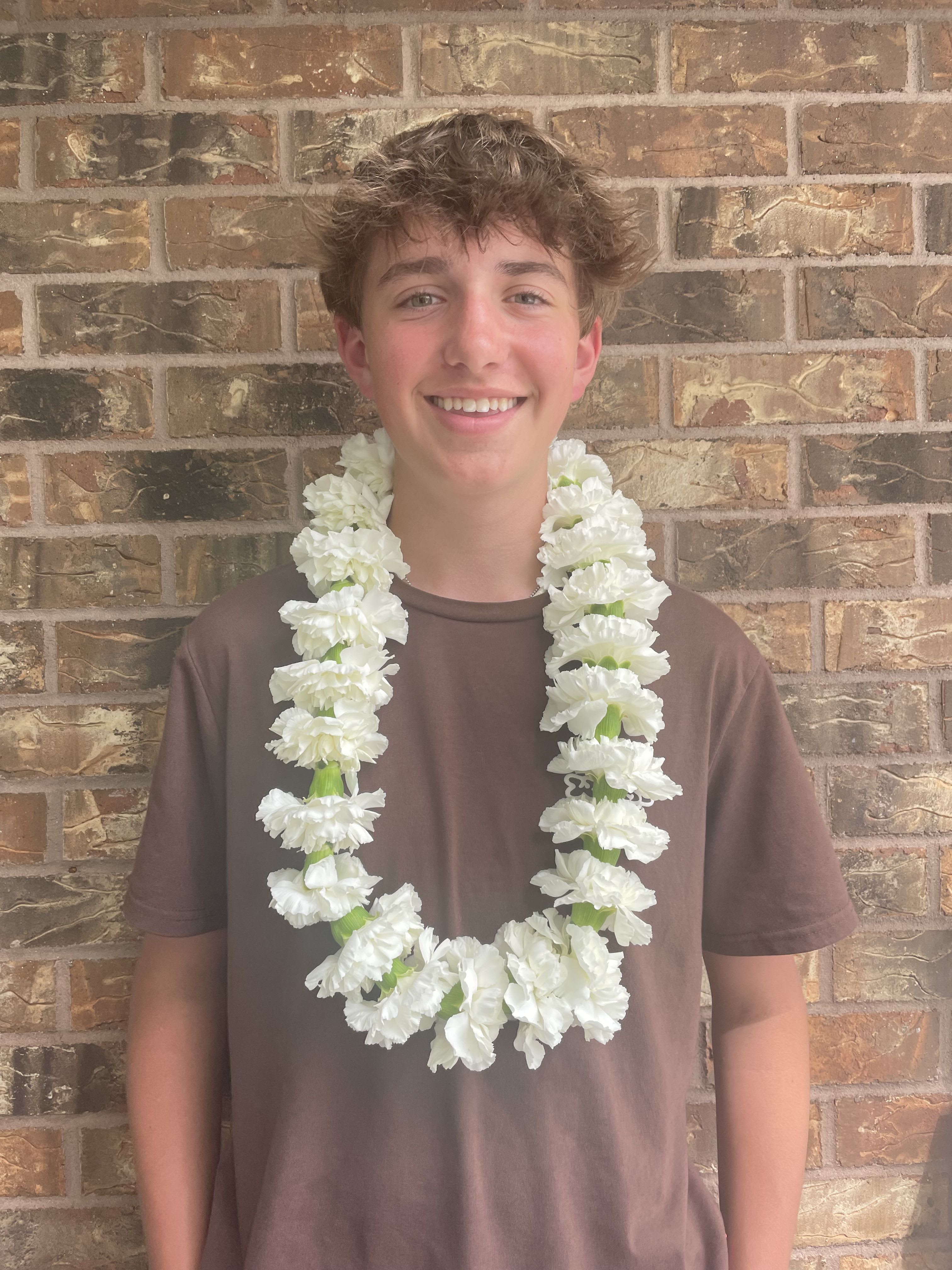Person wearing a white flower lei over a brown shirt