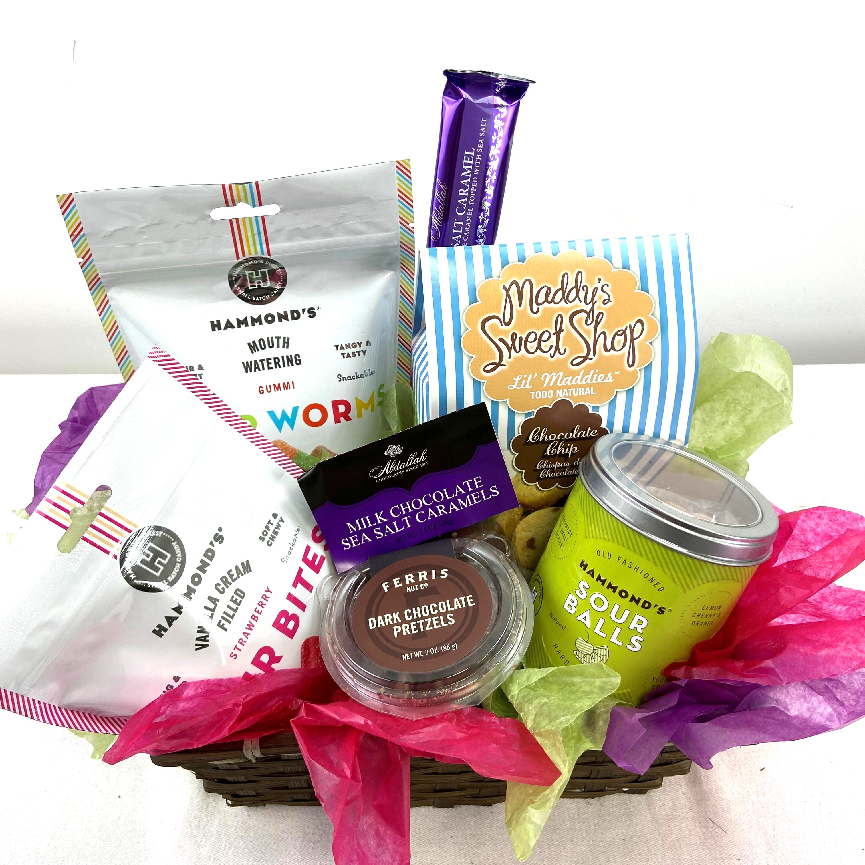 Sweet Snack Basket - A playful assortment of treats arranged in a low woven basket, this Sweet Snack Basket is a cheerful gift for birthdays, thank-you gestures, or a thoughtful just-because surprise. Sweets may vary!  Inside you'll find an assortment of candy and chocolate, all nestled in colorful tissue paper. The contents are arranged casually for easy access and wrapped in clear cellophane with a large bow and curled purple ribbon for a polished finish.   Perfect for coworkers, friends, or family who love sweets, this basket sends a fun, celebratory message without being formal. Order for same-week occasions or pick it up ready-wrapped-no fuss care or assembly required; simply unwrap and enjoy.  Candy may vary!