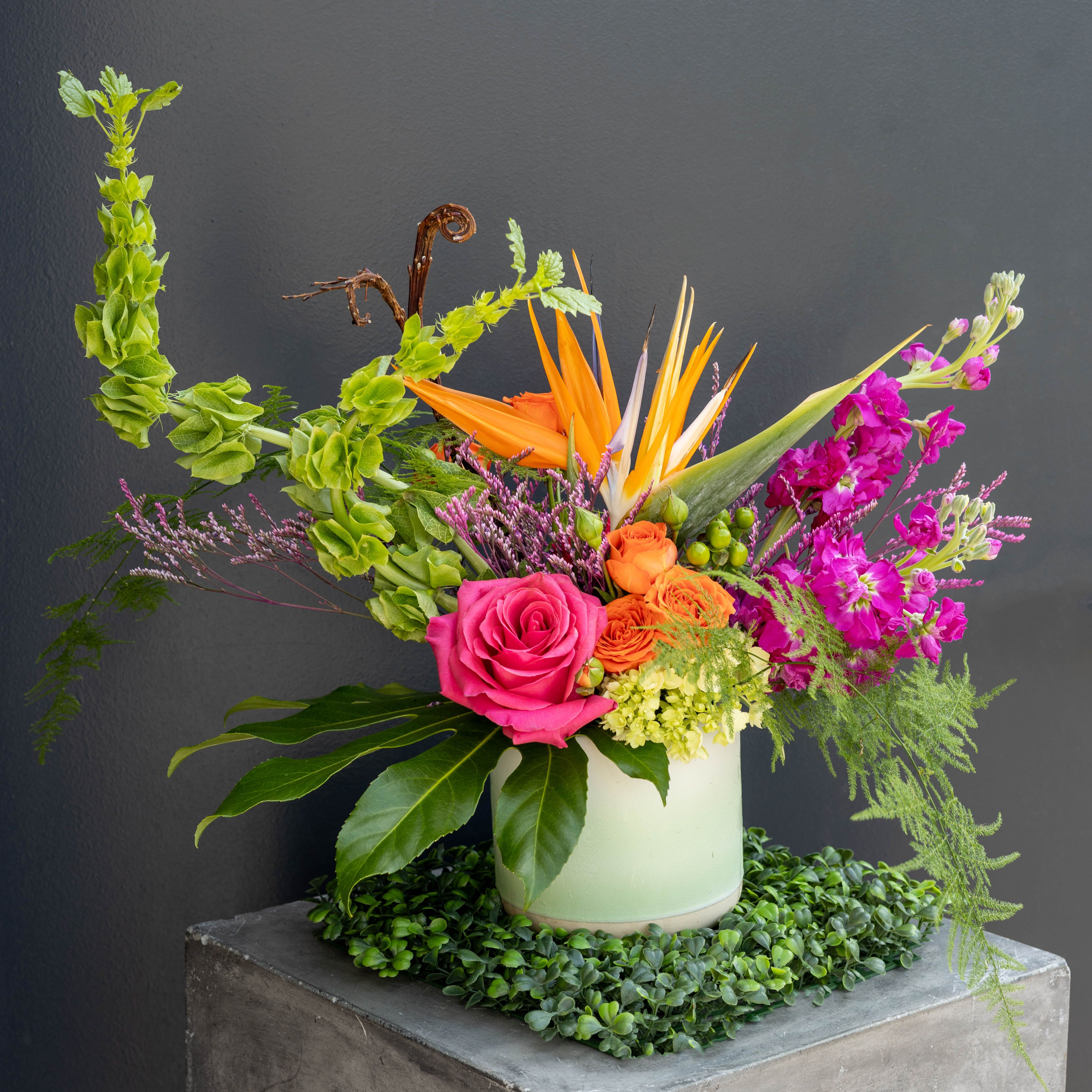 Paradise - Paradise is a striking spring arrangement that instantly transports you to a lush, sun-soaked escape. Bursting with vivid hues of hot pink, citrus orange, and fresh green, this design captures the energy and beauty of exotic blooms in full expression.  Perfect for celebrations, statement pieces, or anyone who loves bold, joyful florals, Paradise brings a little getaway into everyday life, no passport required.