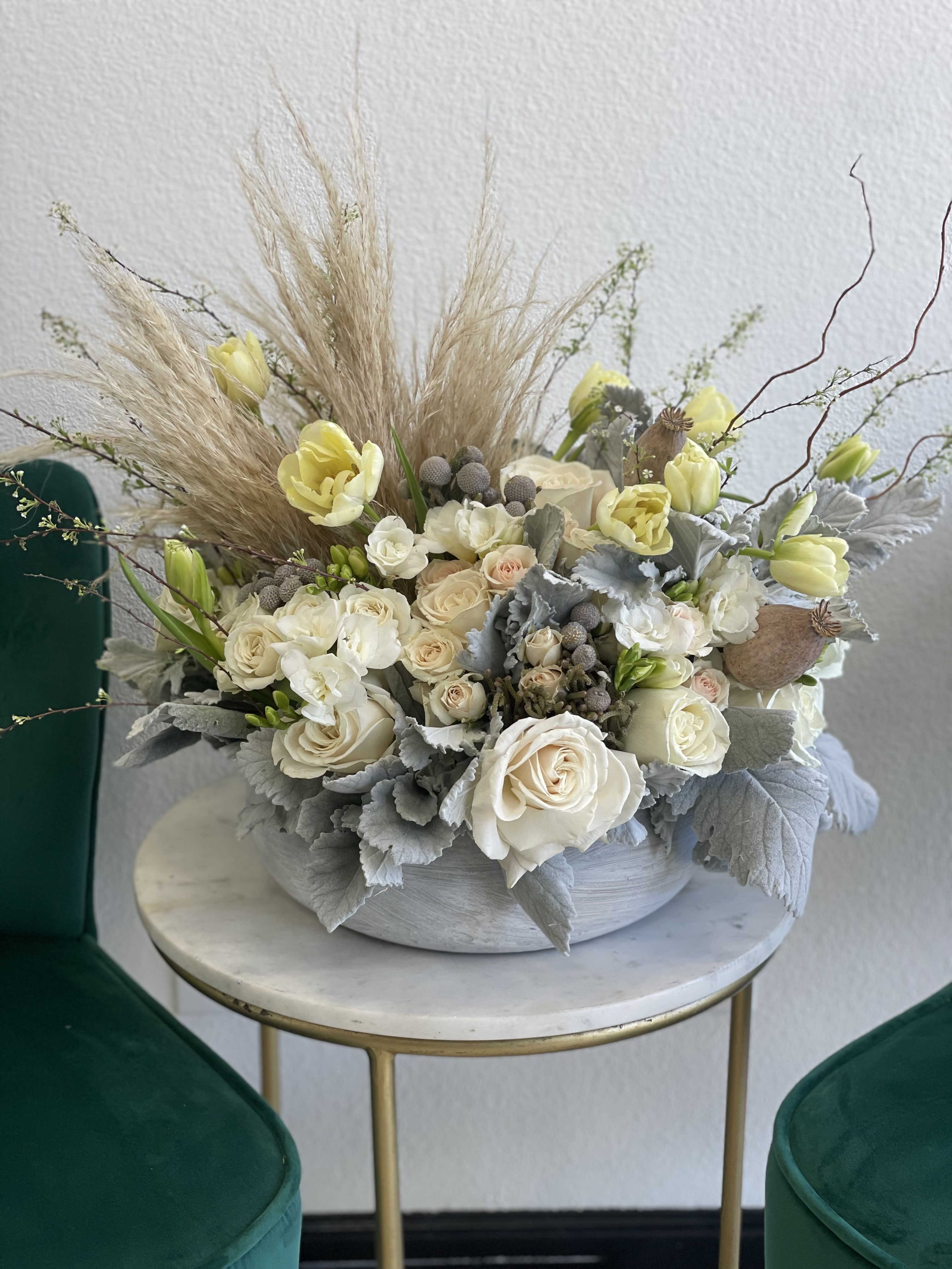 Cream roses and pale yellow tulips in a low gray bowl with dried grasses