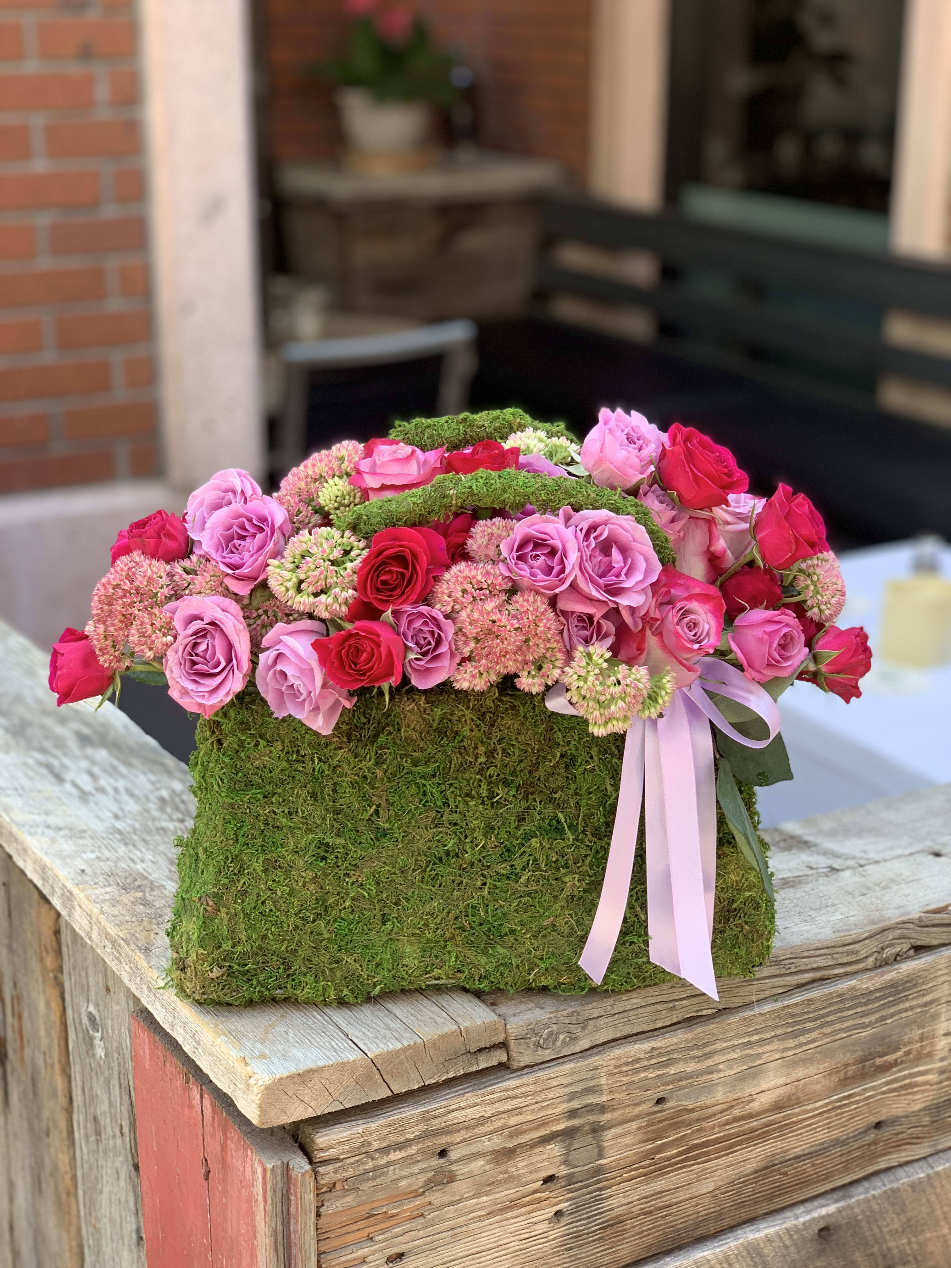 Pink and red roses arranged in a moss-covered box with a ribbon