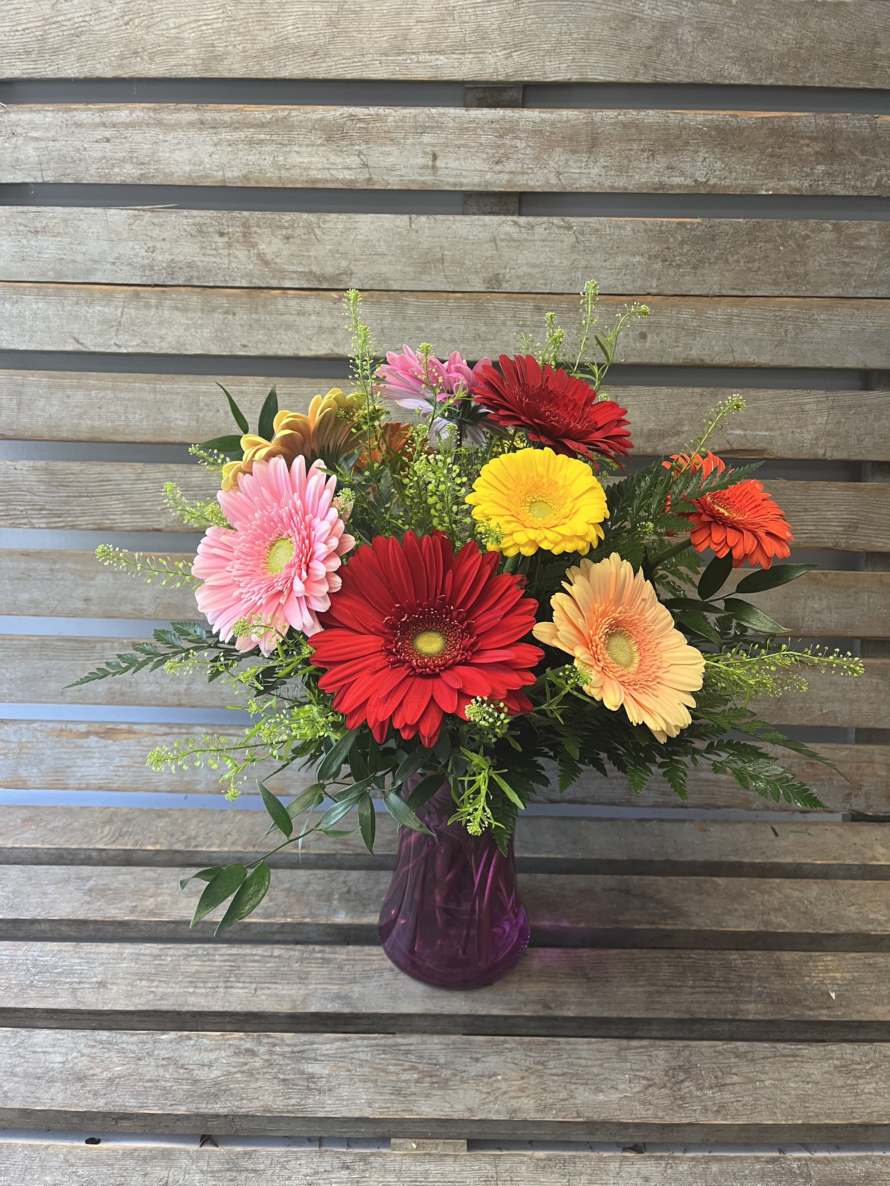 Gerberas for Mom  - Assorted color gerbera daisies with greens and filler in colored or clear gathering vase. Will include a mix of pinks, yellows , oranges and bright colored gerberas. Vase style and color will vary with availability. 