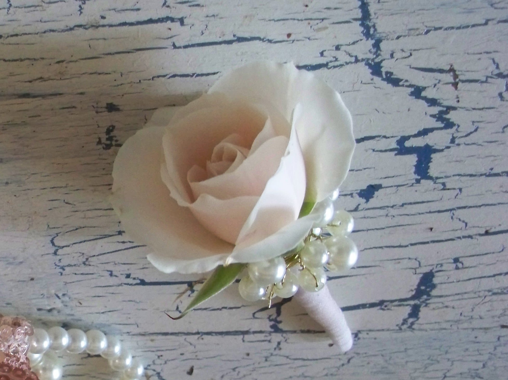 White rose boutonniere with pearl accents on a wrapped stem
