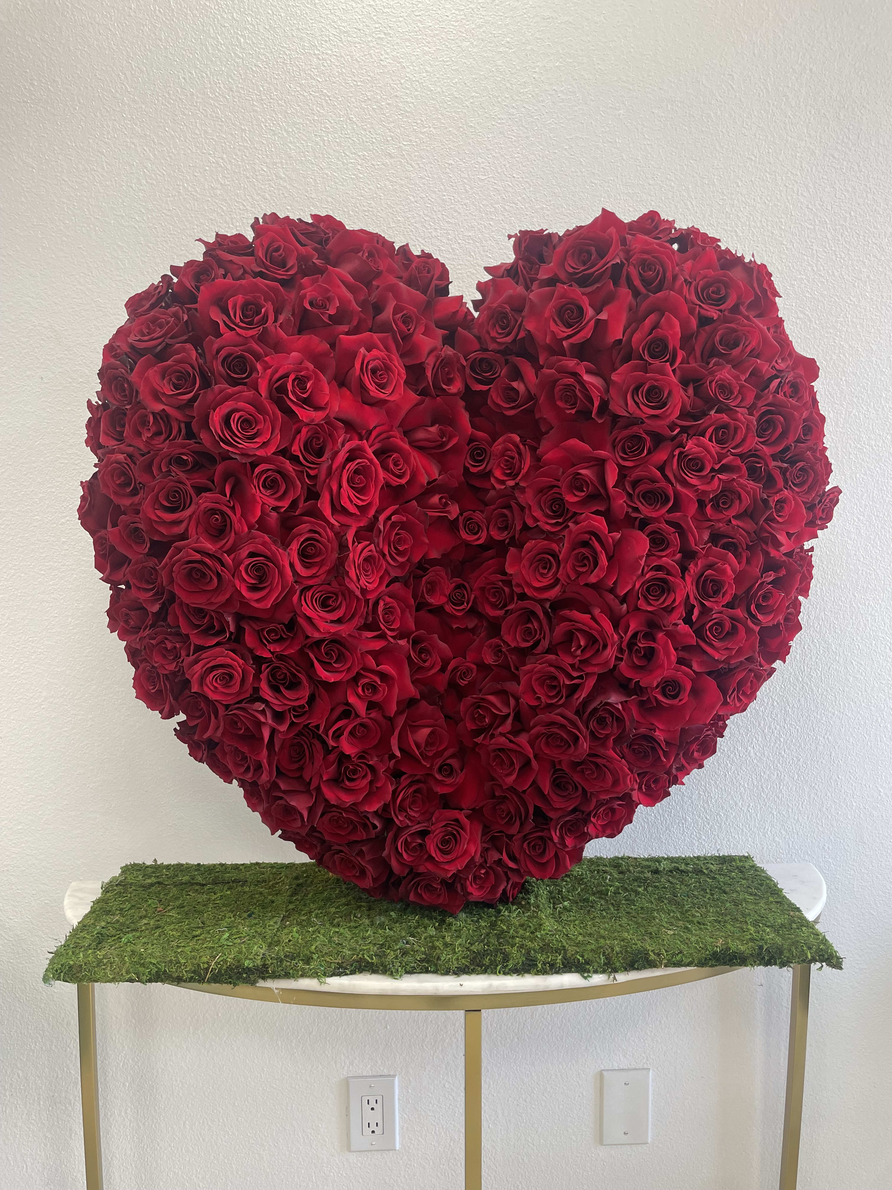 Heart-shaped arrangement of red roses on a moss-covered table