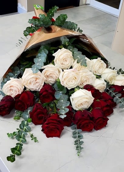 Long bouquet of red and cream roses wrapped in brown paper with eucalyptus accents