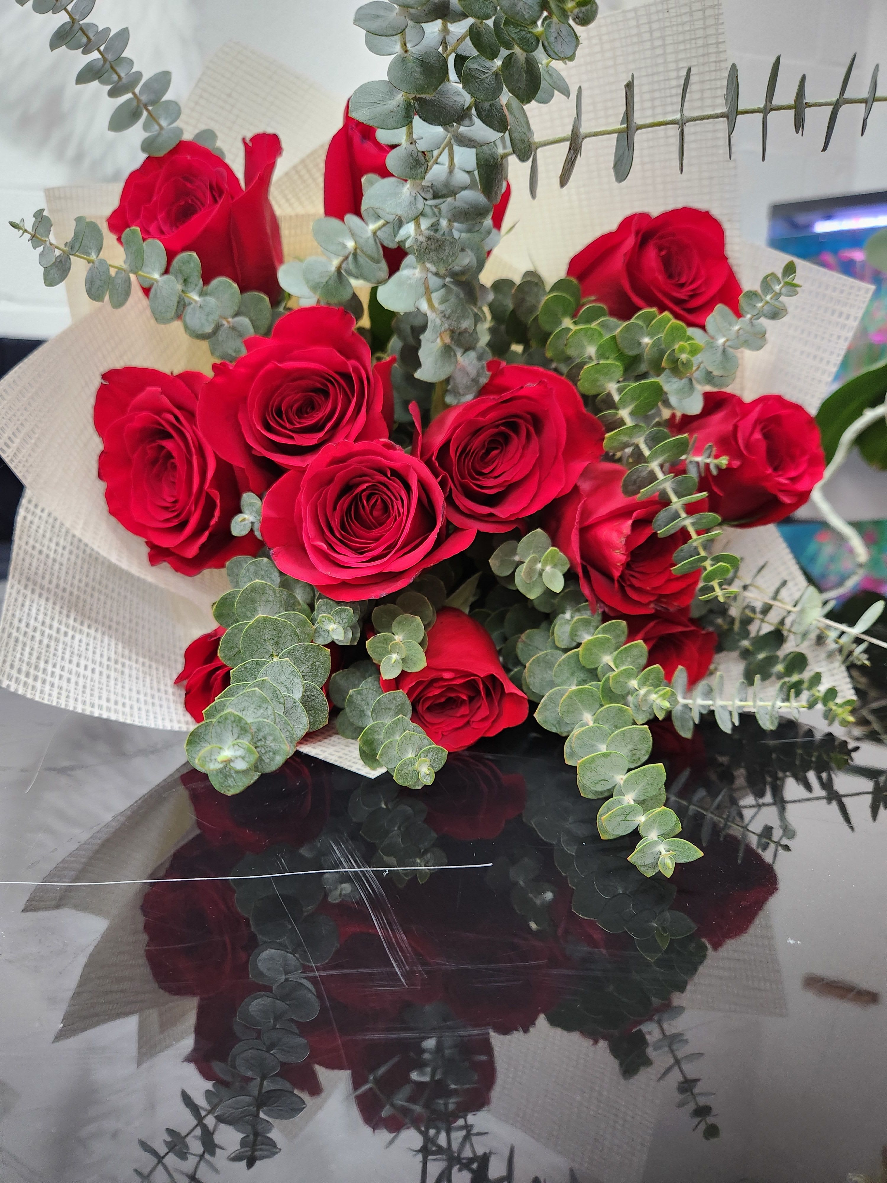 Hand-tied bouquet of red roses with eucalyptus accents wrapped in cream textured paper