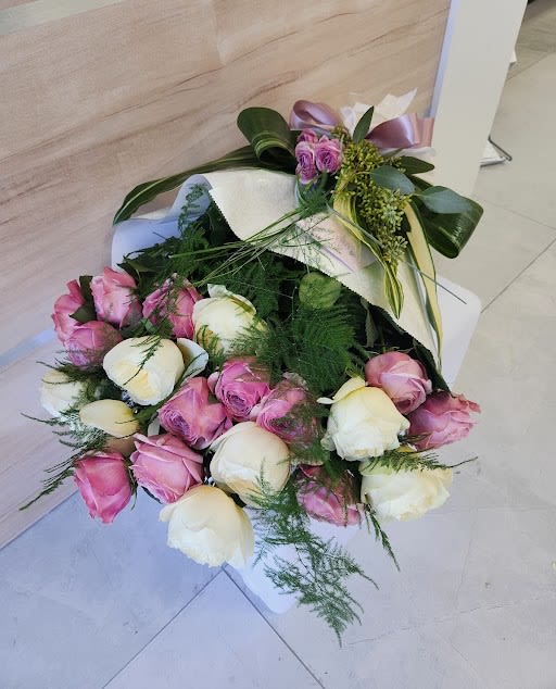 Bouquet of pink and cream roses wrapped in white paper with a satin ribbon bow
