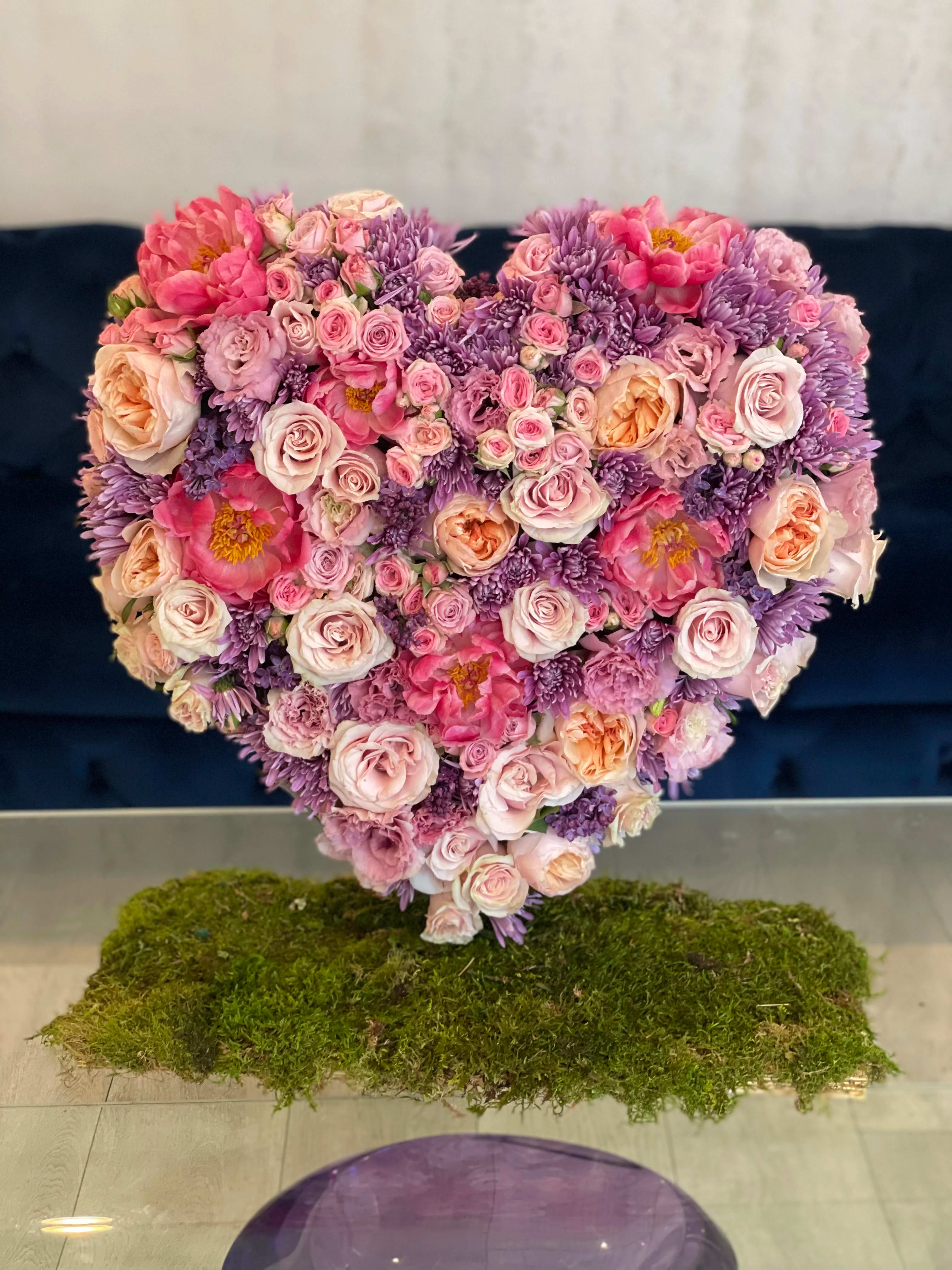 Heart-shaped bouquet of pink and purple flowers on a moss base