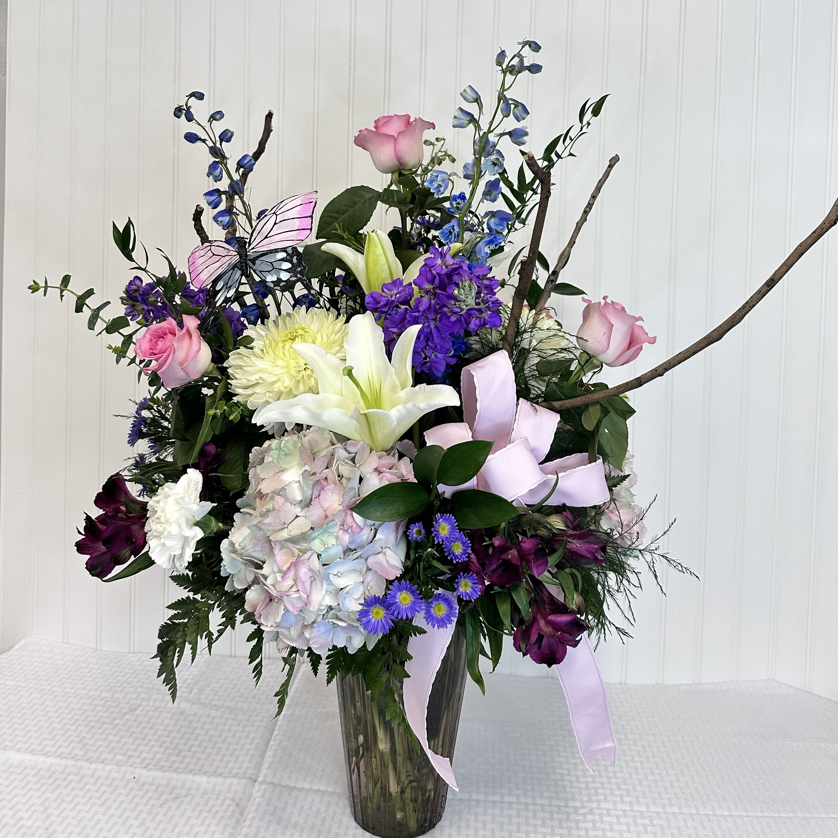 The Sara - The Sara is a timeless masterpiece for Mother's Day. The gorgeous arrangement is sure to melt Mom's heart with beautiful pastel colors and filled with Cotton Candy Hydrangeas, Pink Roses, Delphinium, Chrysanthemums, Carnations &amp; accent flowers.