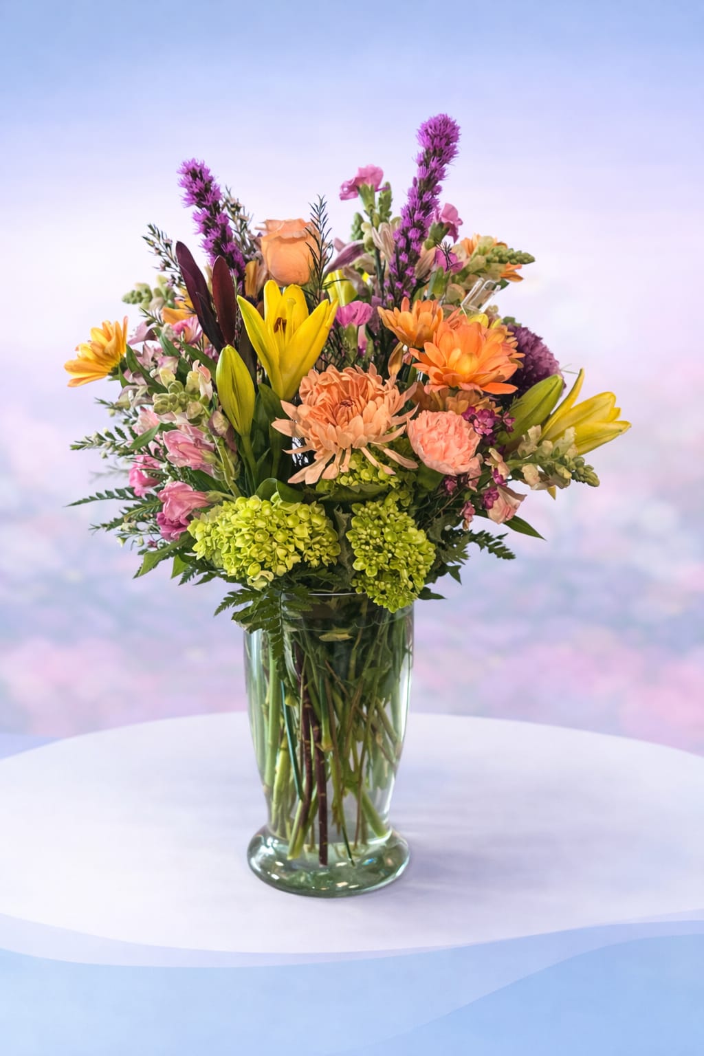 Sunset Garden Party - Bright, bold, and full of life—Sunset Garden Party is a vibrant mix of cheerful blooms that feels like golden hour in a vase. Featuring sunny yellow lilies, peach and coral roses and mums, pops of playful pinks, and fresh green hydrangea, this arrangement is designed with movement and texture for a naturally gathered, garden-inspired look.  Perfect for celebrations, birthdays, or just because, this design brings warmth, color, and energy into any space—thoughtfully arranged to spread joy and, as always, Love Delivered. 