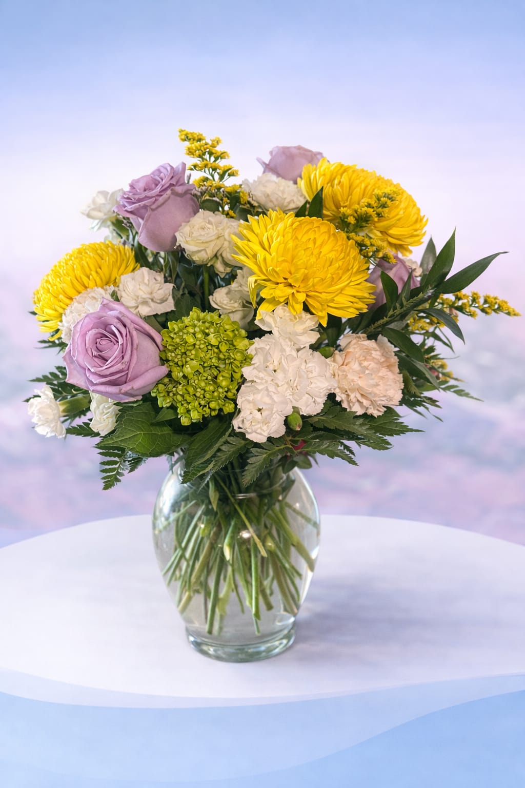 Golden Lavender Garden - Soft, elegant, and full of gentle charm—Golden Lavender Garden blends buttery yellow mums with dreamy lavender roses, creamy carnations, and fresh green hydrangea for a beautifully balanced design. Accented with delicate golden filler and lush greenery, this arrangement has a light, garden-fresh feel with a touch of sophistication.  Perfect for sending comfort, celebrating a special moment, or simply brightening someone’s day, this design brings together warmth and grace in every stem—Love Delivered. 
