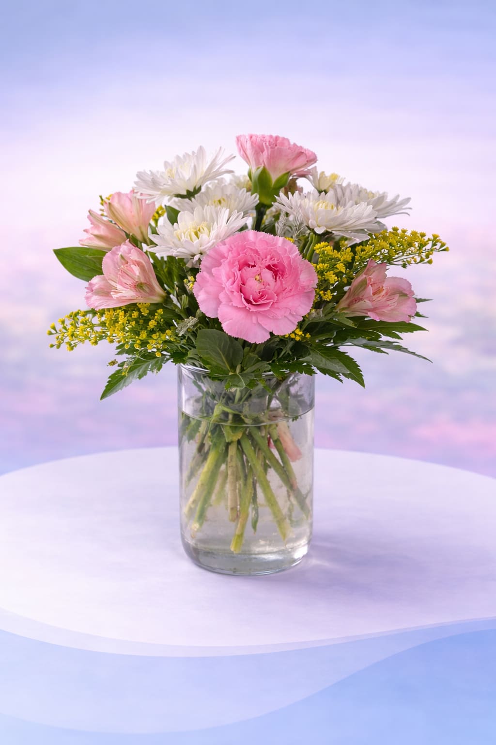 Blushing Daisy Delight - Soft, sweet, and effortlessly cheerful—Blushing Daisy Delight features a beautiful mix of pink carnations, crisp white daisies, and delicate blush alstroemeria, accented with airy golden filler and fresh greenery. Designed in a simple glass vase, this arrangement has a light, garden-fresh feel that’s both classic and uplifting.