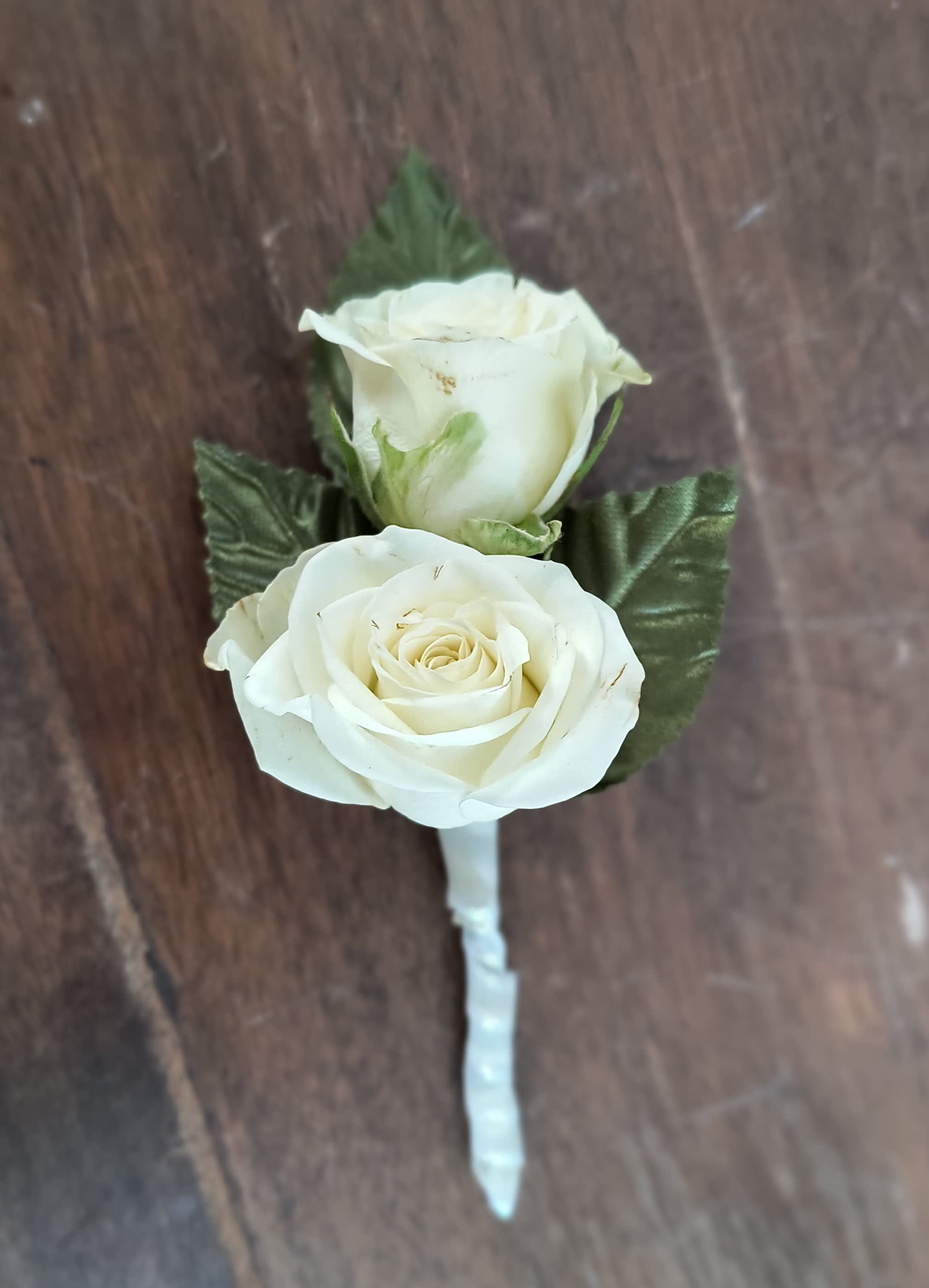 White rose boutonniere with green leaves on a wrapped stem
