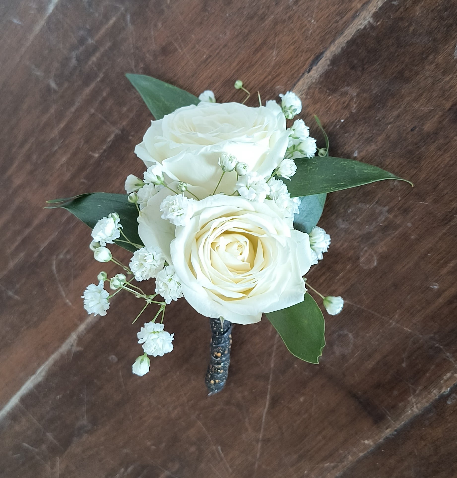 White rose boutonniere with baby's breath and green leaves