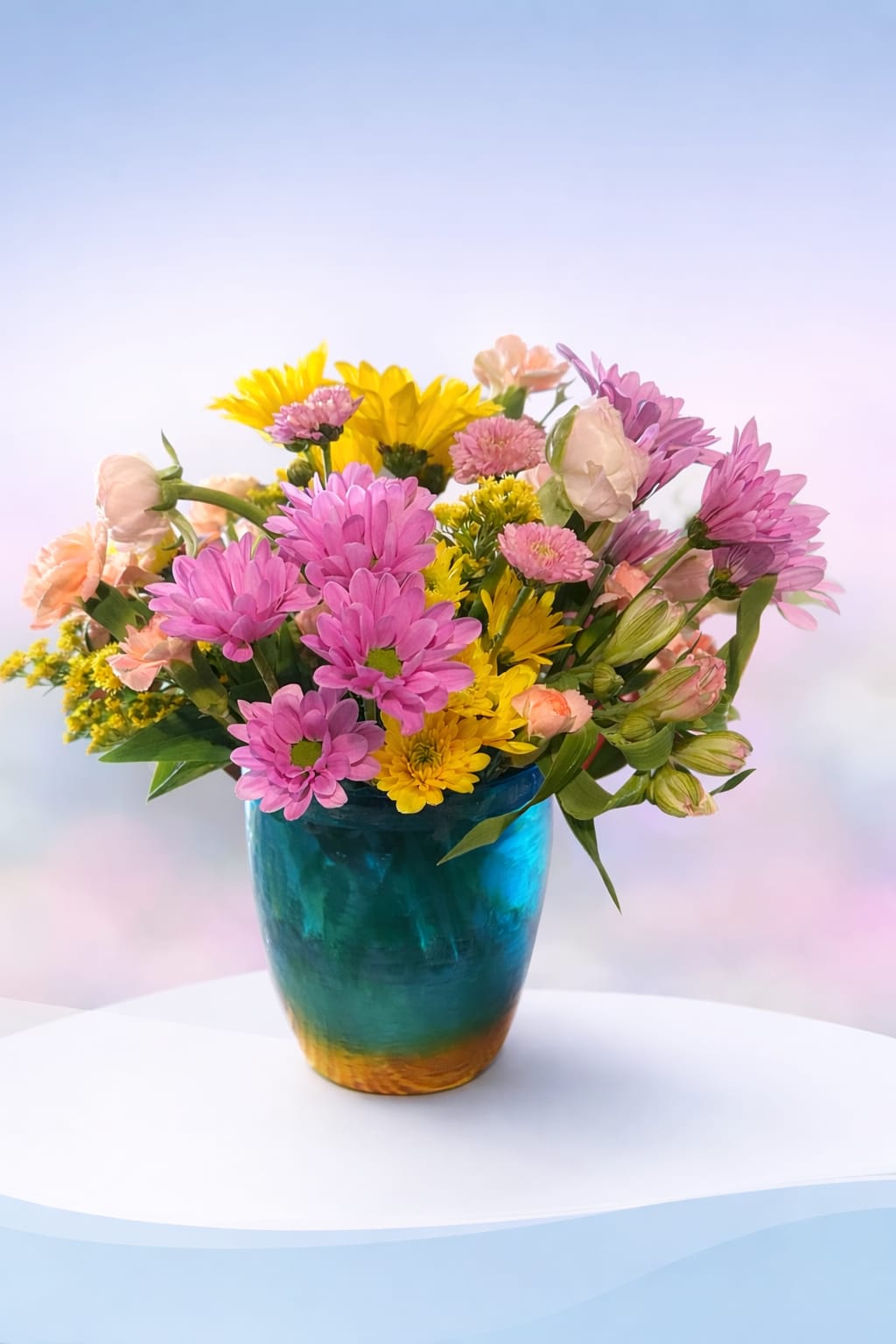 Ranunculus Garden Pop - Bright, cheerful, and full of playful color—Ranunculus Garden Pop features a lively mix of pink and yellow blooms accented by soft peach ranunculus that add a touch of delicate, layered elegance. Surrounded by fresh greenery and garden-style textures, this arrangement feels light, fun, and effortlessly inviting.