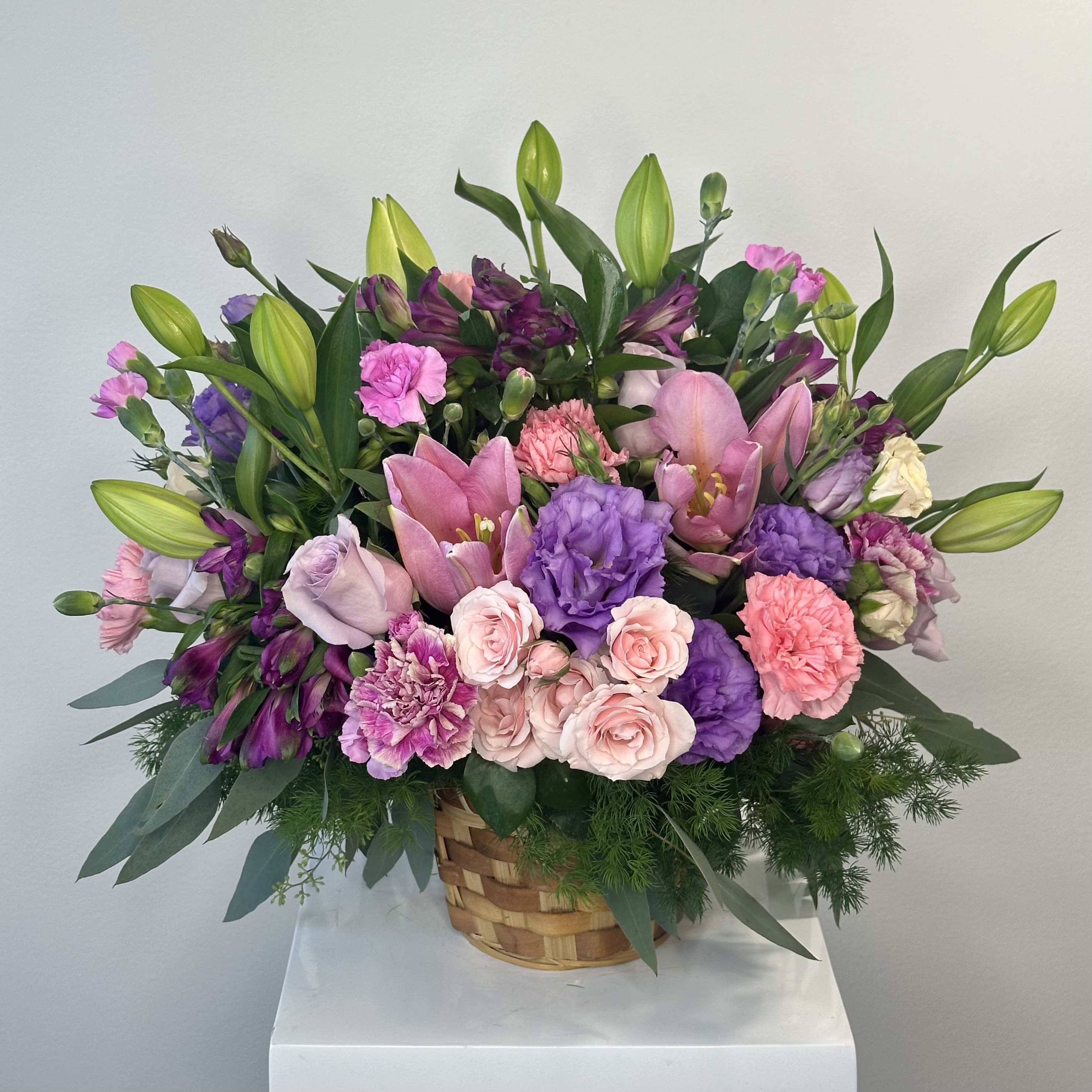 Loving Out Loud - Discover the vibrant and heartfelt Loving Out Loud flower arrangement – a bold, joyful celebration of love wrapped in a charming woven wicker basket. This stunning basket arrangement bursts with rich purples and soft pinks, blending romantic elegance with playful energy. Perfect for anniversaries, Valentine's Day, birthdays, Mother's Day, or as a heartfelt "I love you" gift that truly speaks volumes. The design shines with elegant purple lisianthus, offering delicate, rose-like petals and lasting sophistication. Velvety purple roses bring luxurious passion and timeless romance, while abundant clusters of pink spray roses add delightful texture and softness. Graceful pink lilies provide fragrant height and striking beauty, paired with cheerful alstroemeria (Peruvian lilies) in lively pink hues for vibrant, long-lasting freshness. Fluffy pink carnations complete the look with classic charm, volume, and enduring appeal. Nestled in a handwoven wicker basket, this arrangement exudes rustic warmth and natural elegance – ideal for tabletop displays, home decor, or thoughtful surprises. Expertly hand-arranged by skilled florists with the freshest blooms, Loving Out Loud arrives ready to delight in its beautiful basket container. Express your feelings boldly with this purple and pink floral masterpiece. Order Loving Out Loud today for same-day or scheduled delivery and watch love bloom vibrantly!