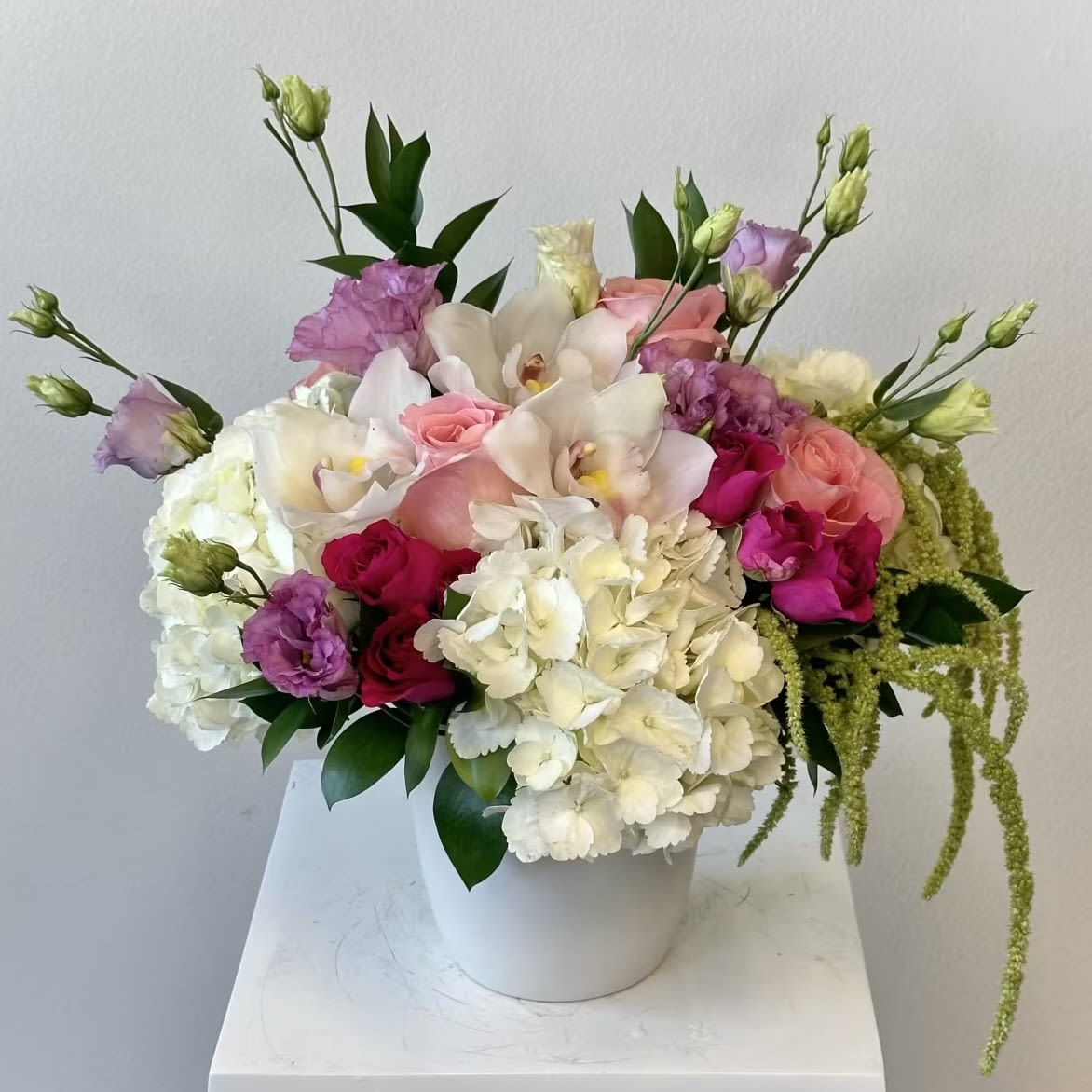 Sweet Pea - Sweet Pea Flower Arrangement – Elegant White Hydrangea &amp; Orchid Bouquet with Pink Roses Indulge in timeless romance with the “Sweet Pea” flower arrangement, a luxurious cascade of soft whites, blush pinks, and regal purples. Anchored by fluffy white hydrangeas and exotic white cymbidium orchids, this masterpiece weaves in delicate purple lisianthus, classic pink roses, vibrant fuchsia spray roses, and trailing hanging amaranthus for dramatic, garden-inspired movement. Perfect for weddings, anniversaries, or sophisticated sympathy tributes.  Highlights of Sweet Pea: White Hydrangeas: Lush, cloud-like blooms symbolize gratitude and heartfelt emotion. White Cymbidium Orchids: Rare, long-lasting elegance with a tropical flair. Purple Lisianthus: Ruffled petals add depth, grace, and a touch of royalty. Pink Roses: Timeless symbols of admiration, joy, and gentle love. Fuchsia Spray Roses: Playful clusters deliver bold color and texture. Hanging Amaranthus: Cascading “love-lies-bleeding” tails create stunning vertical drama.  Nestled in a sleek ceramic vase. Ideal for bridal bouquets, luxury home décor, or “thinking of you” gestures. Sweet pea flower arrangement, white hydrangea bouquet, cymbidium orchid delivery, purple lisianthus roses, pink fuchsia spray roses, hanging amaranthus floral design, luxury wedding flowers, anniversary orchid bouquet, sympathy white flowers, same-day elegant flower delivery. Elevate any occasion with “Sweet Pea” – order now for same day delivery! 