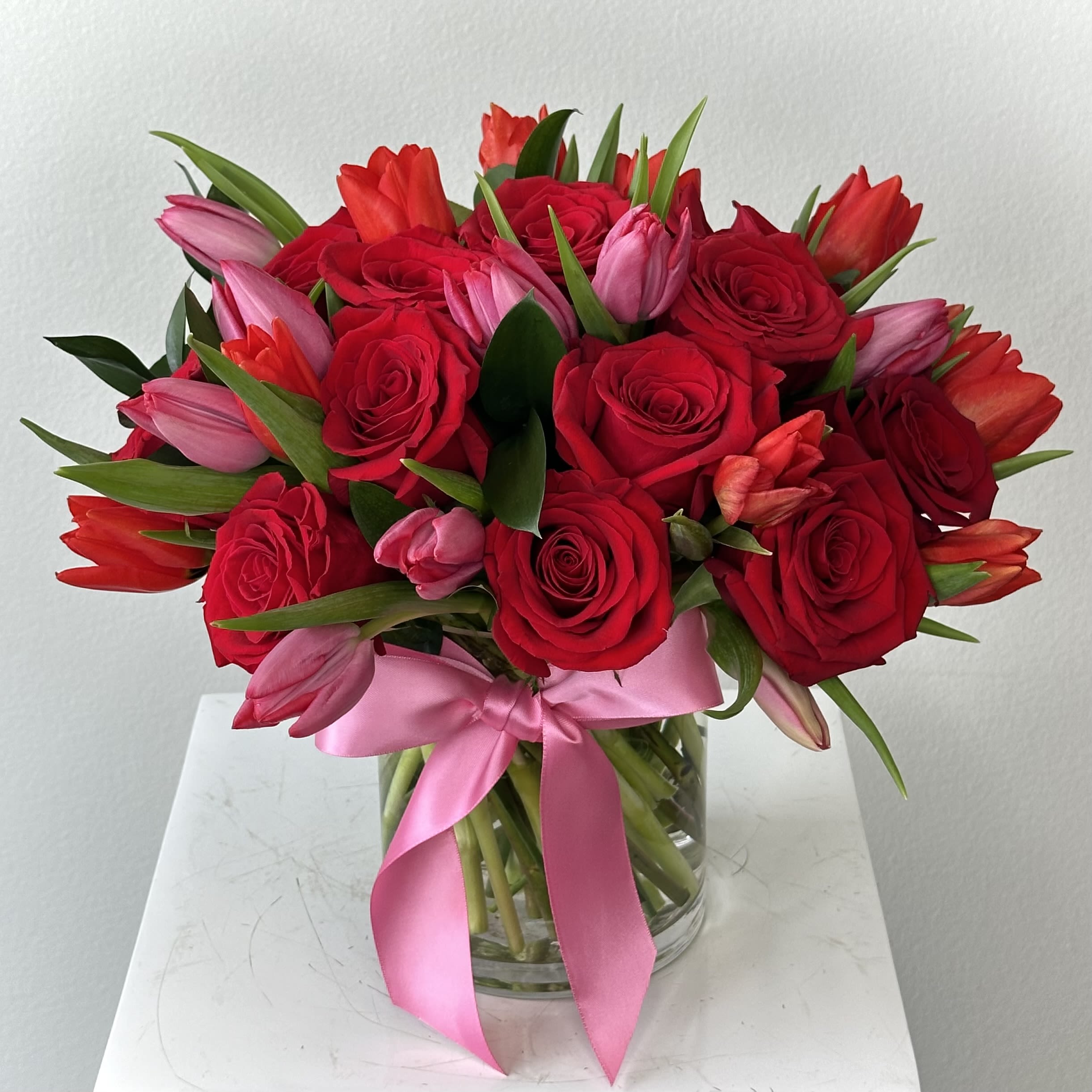 Bouquet of red roses and pink tulips in a glass vase with a pink ribbon