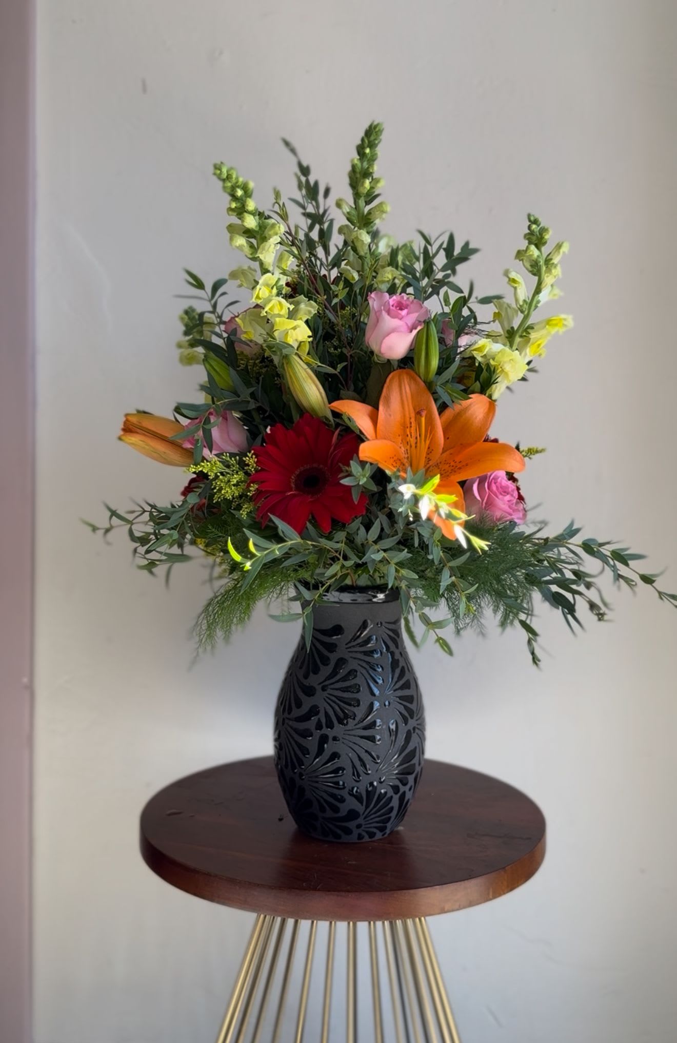 Mixed bouquet in a black vase with lilies, roses, and a red gerbera daisy