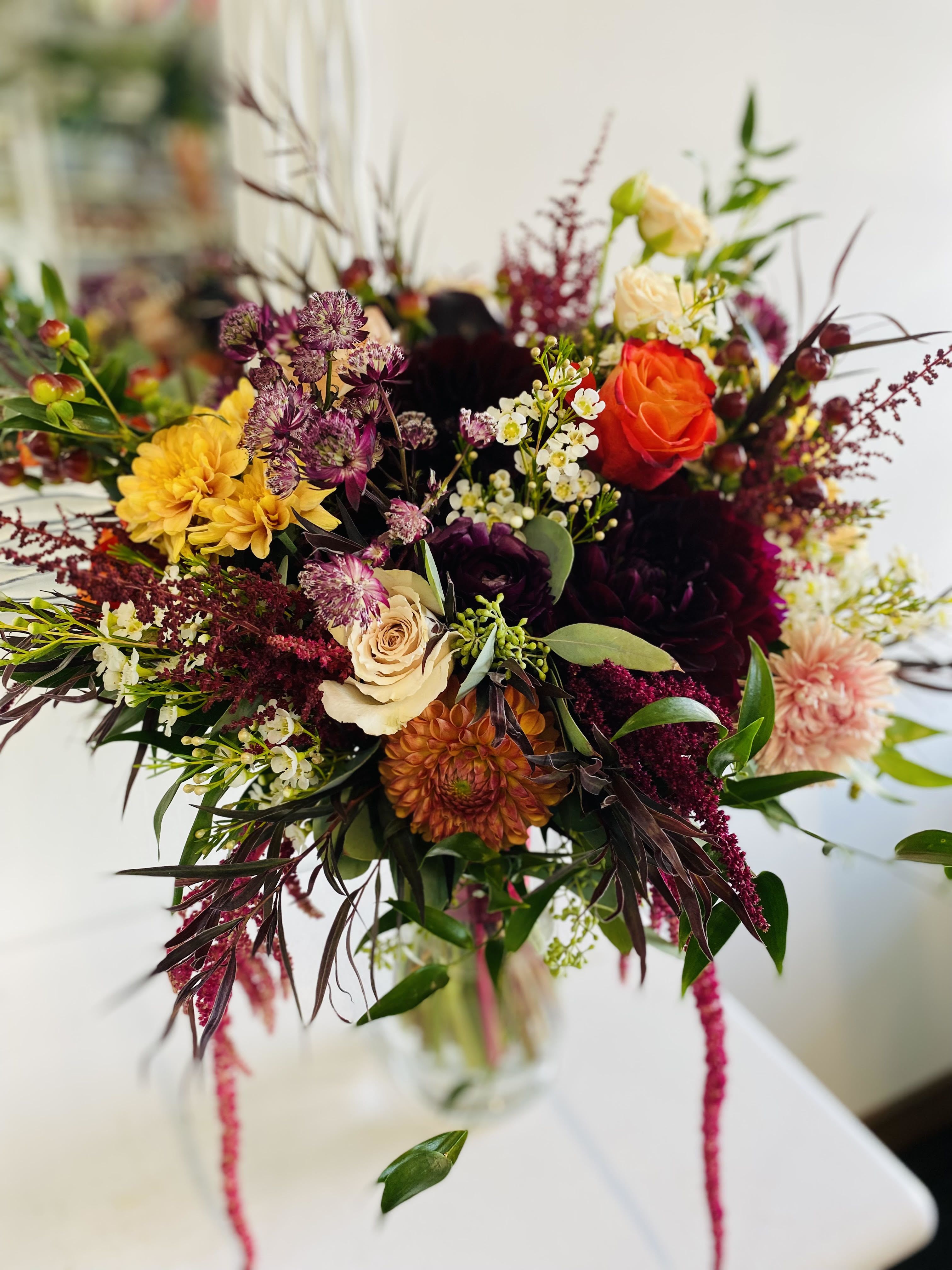 Mixed bouquet of orange, yellow, burgundy, and cream flowers in a glass vase