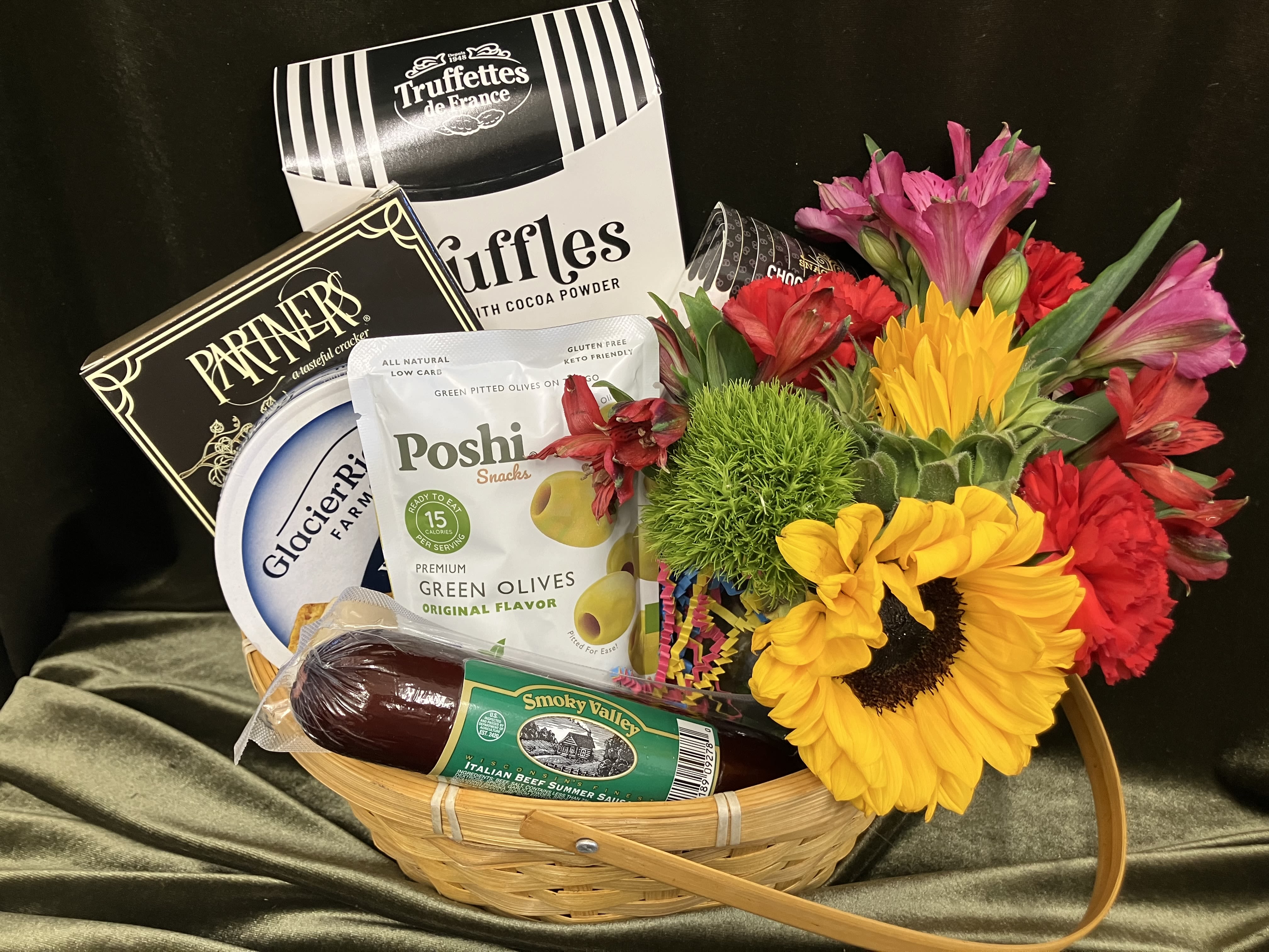 Cute Flowers and Snacks - Imagine a charming small flower and snack gift basket, a delightful combination of nature's beauty and culinary treats. A heart shaped basket, filled with an array of carefully chosen items within the basket, you'll find a small bouquet of delicate flowers, like cheerful sunflowers, carnations, alstroemerias and more. Complementing the floral display are an assortment of delectable snacks, carefully curated to appeal to various tastes. For a sweet tooth, chocolates and a chocolate covered pretzel! Salted crackers offer a satisfying crunch,  and those with a preference for something savory, olives, meat and cheese. The combination of textures and flavors creates a delightful tasting experience.  Together, these elements create a thoughtful and charming gift basket, perfect for brightening your special someones day