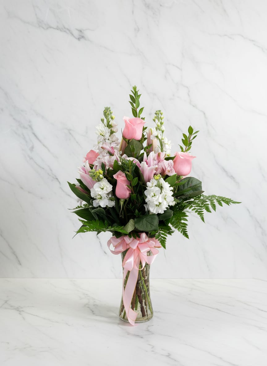 Pink roses and white flowers arranged in a glass vase with a pink ribbon