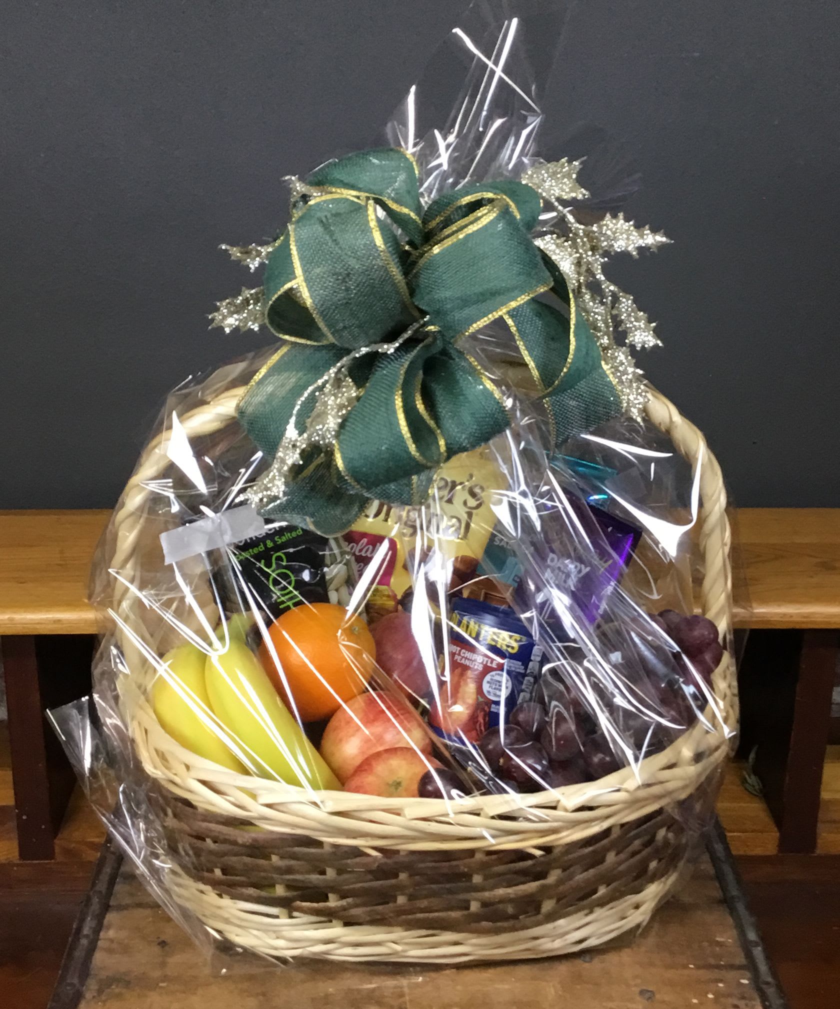 Gift basket with fruit, snacks, and a green ribbon bow