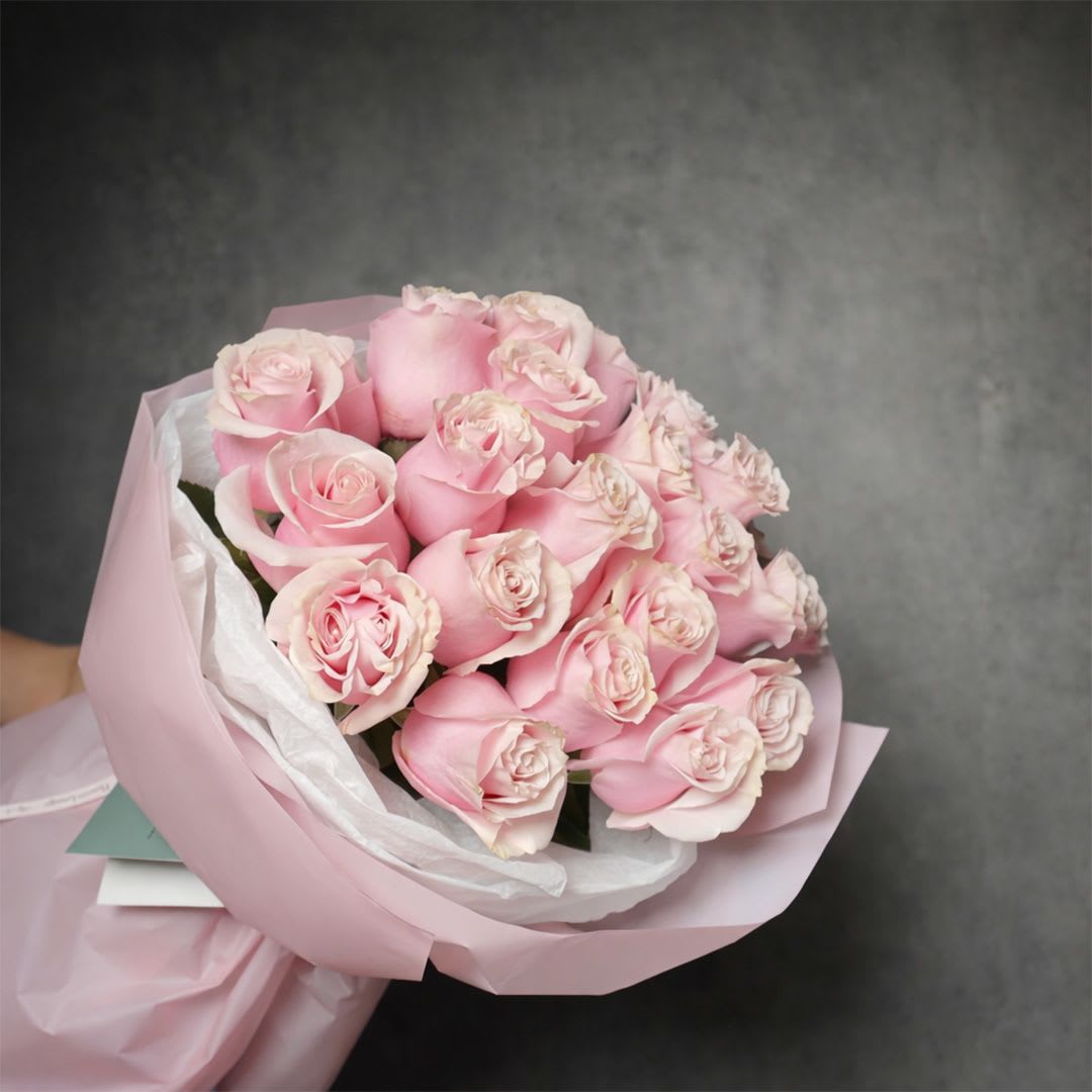 Hand-tied bouquet of light pink roses wrapped in pale pink paper.