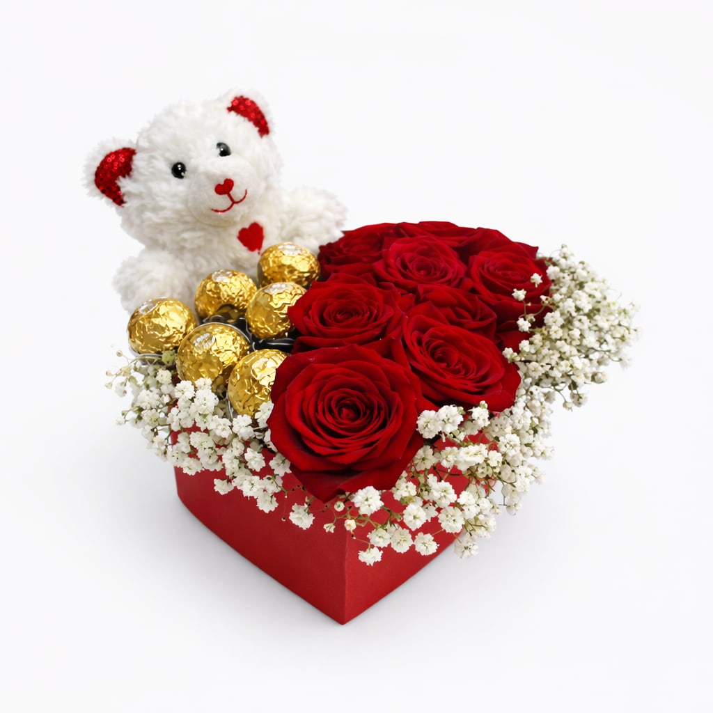 Red roses in a heart-shaped box with a teddy bear and gold chocolates