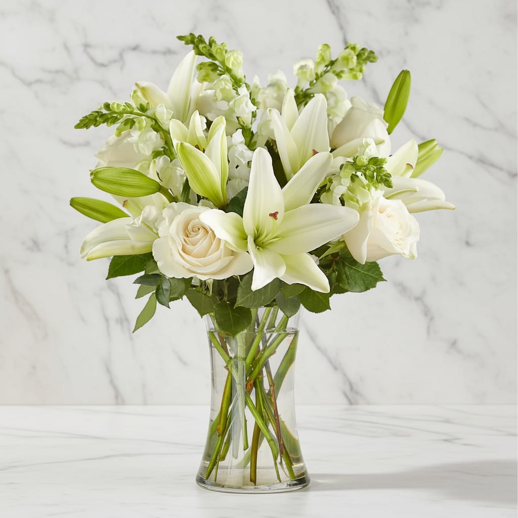 Eternal Friendship Bouquet - An exuberance of bright and beautiful white blossoms provides an exquisite way to deliver your expressions of sympathy and comfort. This life affirming tribute combines white roses, snapdragons and Asiatic lilies accented by lush greens arranged in a clear glass 8" vase. An excellent choice for a wake, funeral service or for sending your condolences to the home of grieving family or friends.