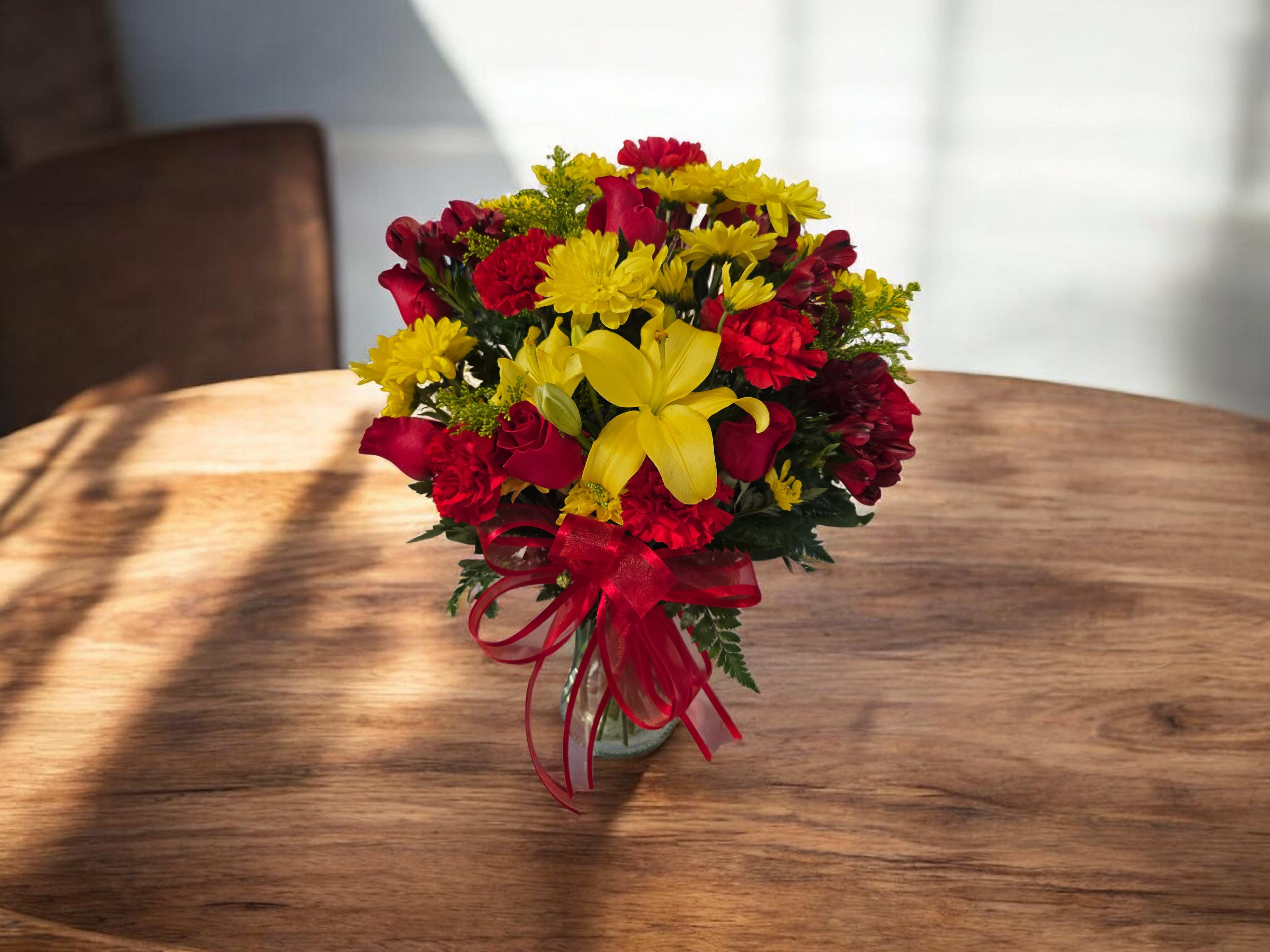 Golden Celebration Bouquet - A vibrant blend of sunny yellow lilies and cheerful daisies paired with rich red blooms, beautifully arranged with lush greenery and a decorative ribbon. Perfect for celebrations, special occasions, or adding a warm, festive touch to any space.