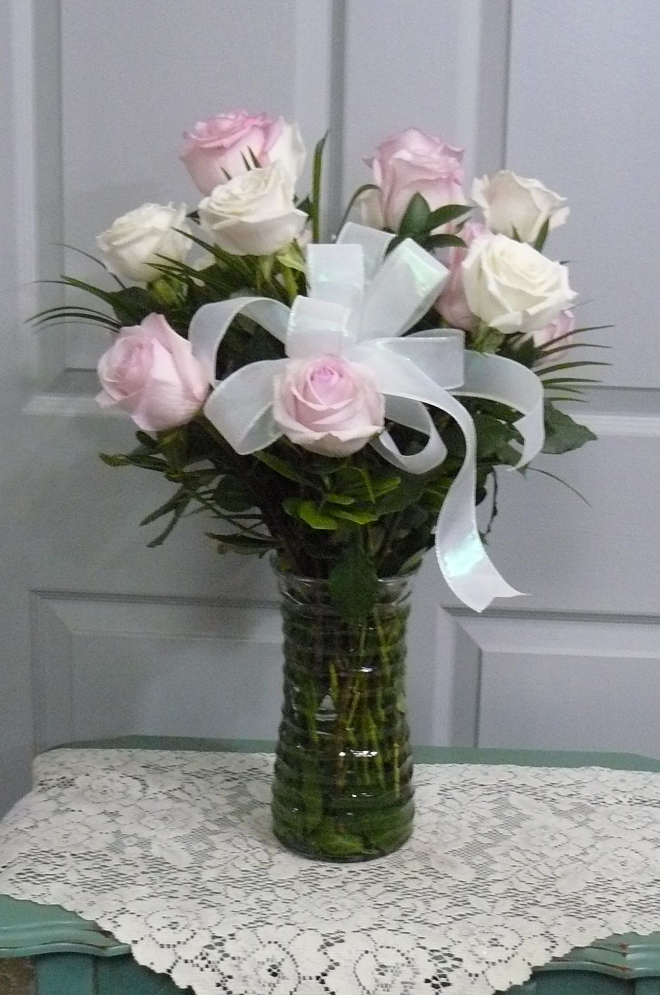 Pink and white roses arranged in a glass vase with a white ribbon