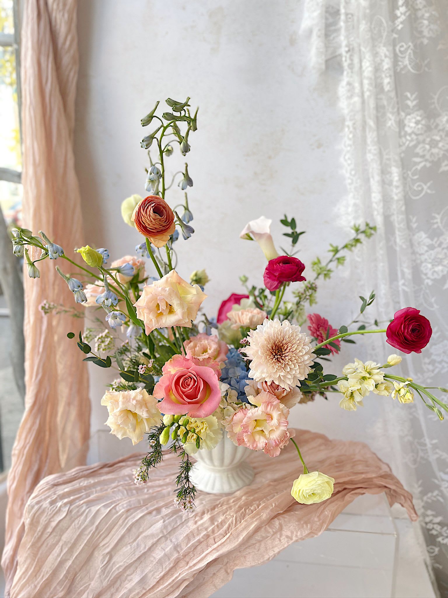 Soft &amp; Sunny - A romantic garden-style arrangement featuring pink roses, ranunculus, lisianthus, and delicate seasonal blooms in soft peach, cream, and airy blue tones. Designed in a classic ceramic compote, this whimsical composition blends texture, movement, and elegance—perfect for spring gifting, home styling, or special occasions in Hoboken and Jersey City.