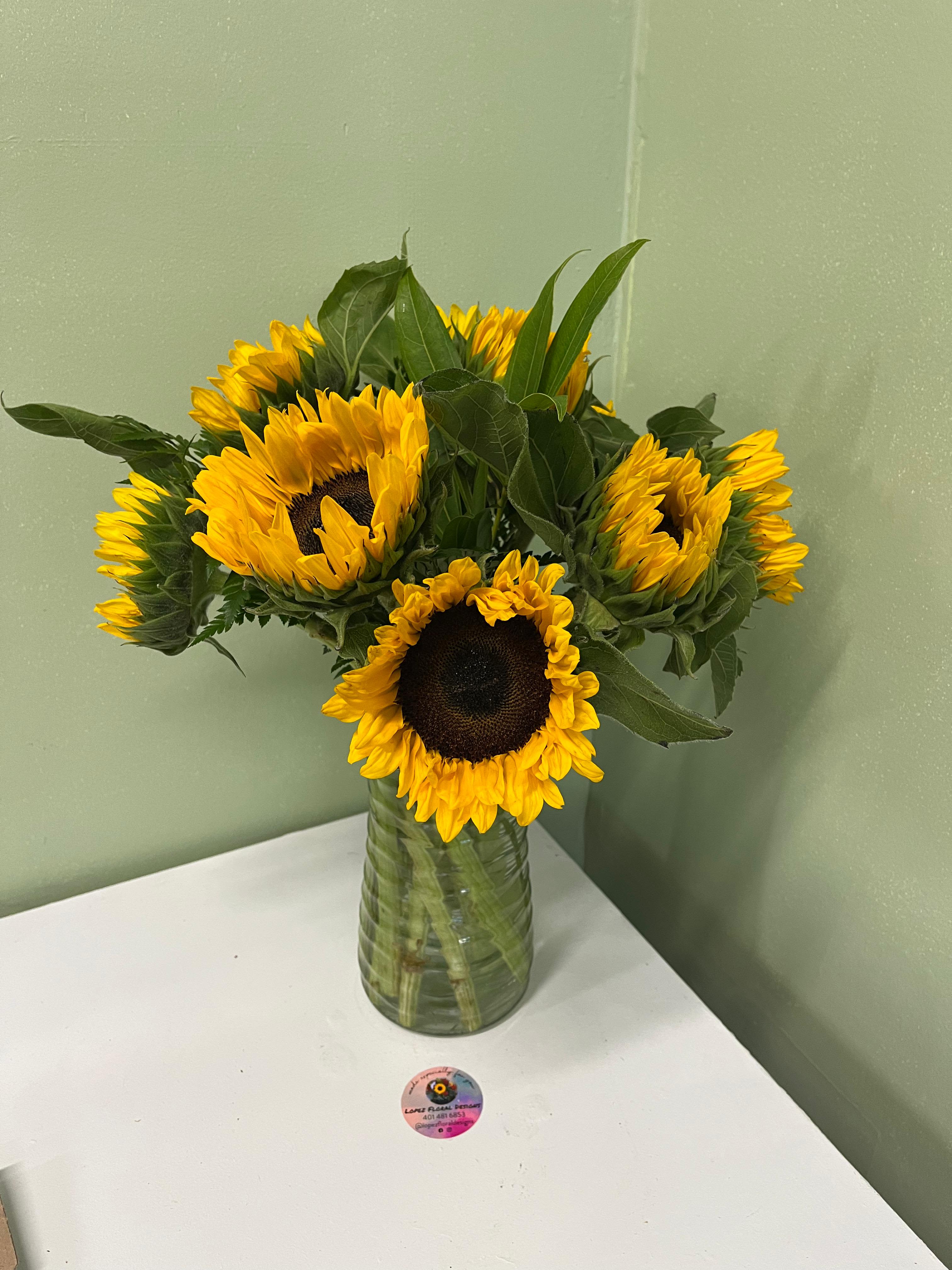Vase arrangement of yellow sunflowers with dark centers in a clear glass vase on a white table